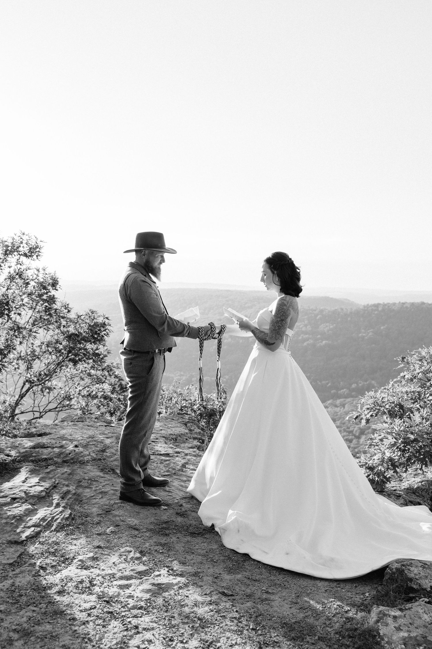 A romantic wedding photoshoot on a mountain cliff showing a couple in black and white against a scenic backdrop.