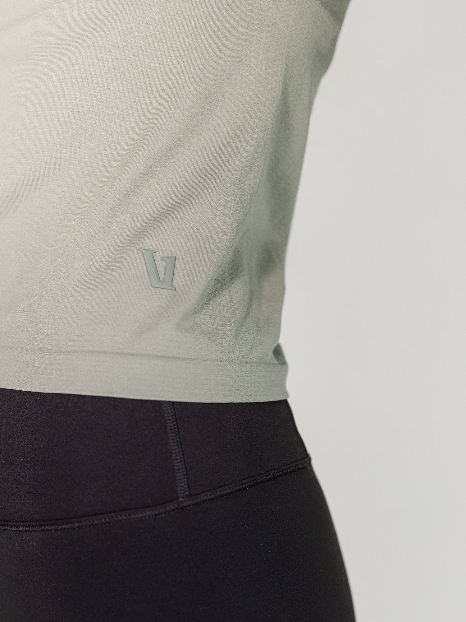 Close-up of a sage green athletic top with subtle logo detail, paired with black leggings.