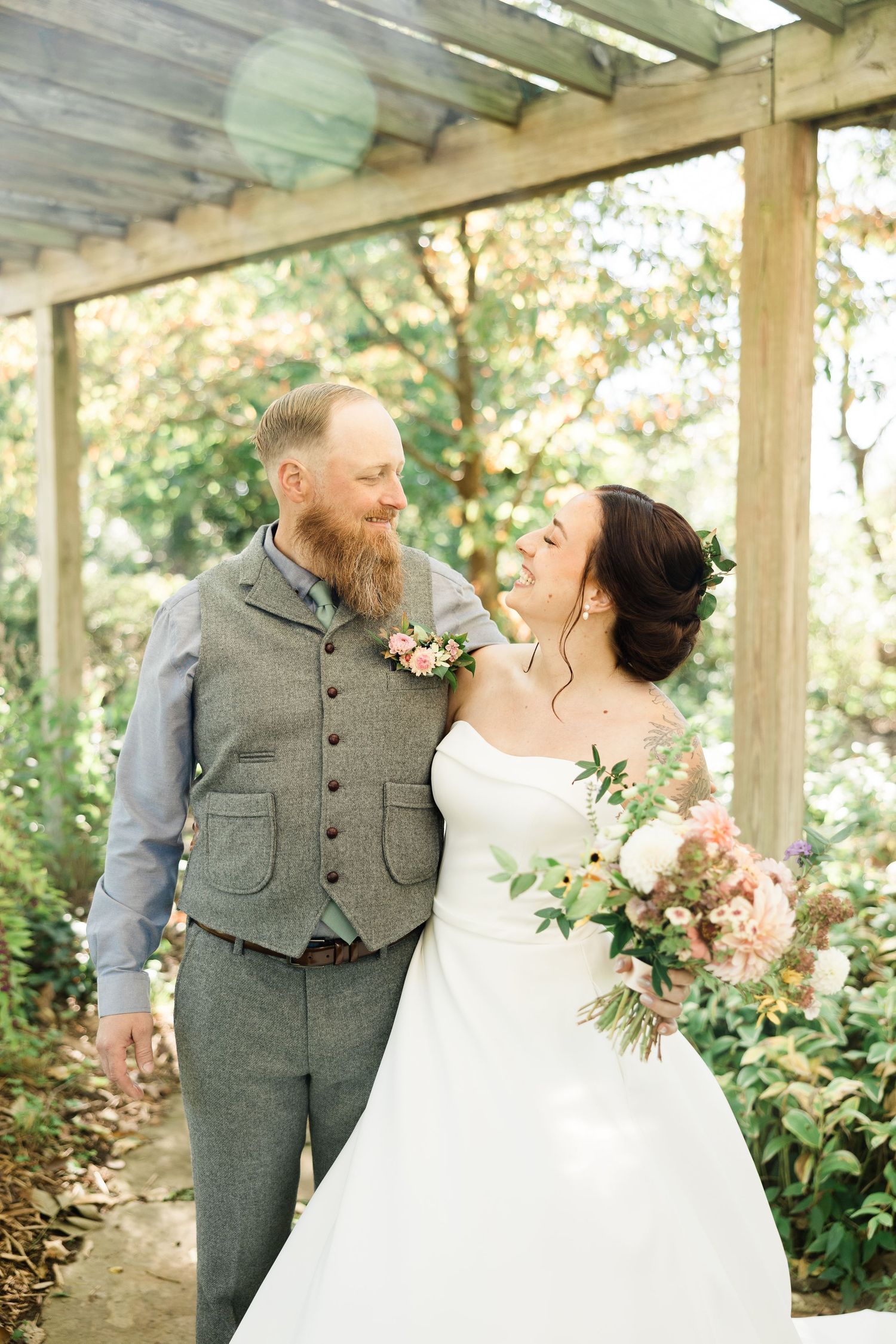 A couple shares a romantic moment in a covered garden setting wearing grey suit and white wedding dress.
