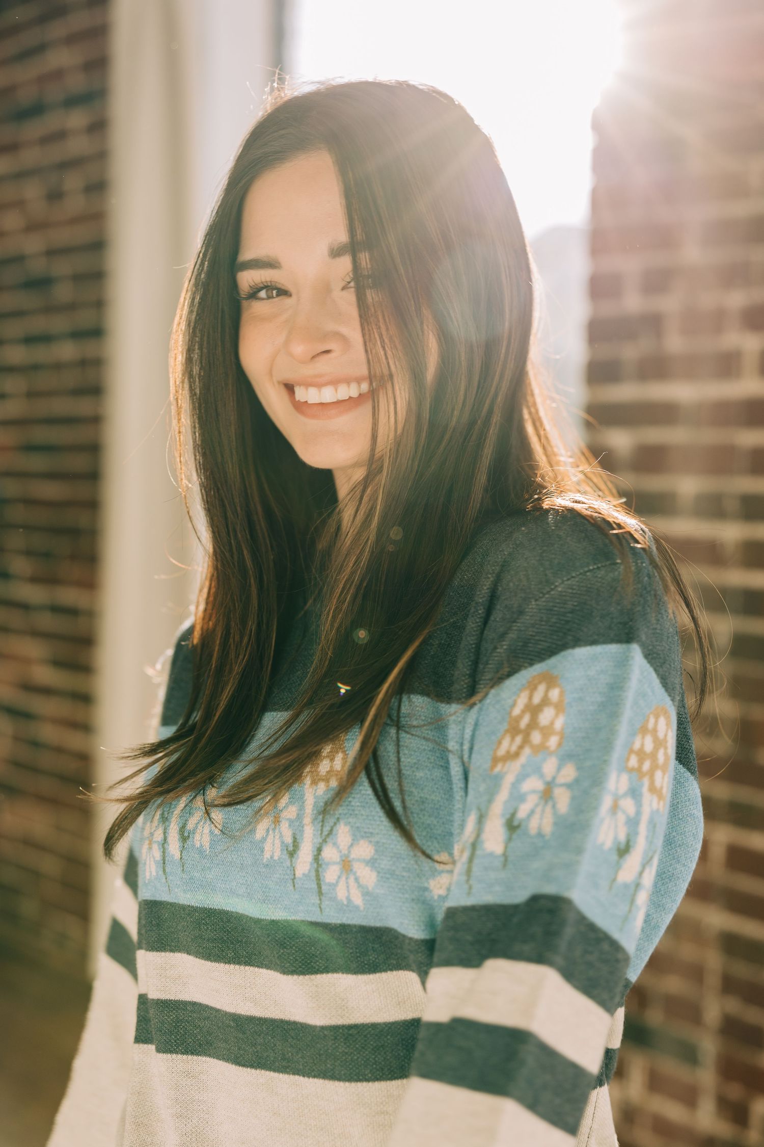 Portrait series showing someone with dark hair wearing a blue and white patterned sweater in warm sunlight against a brick wall.