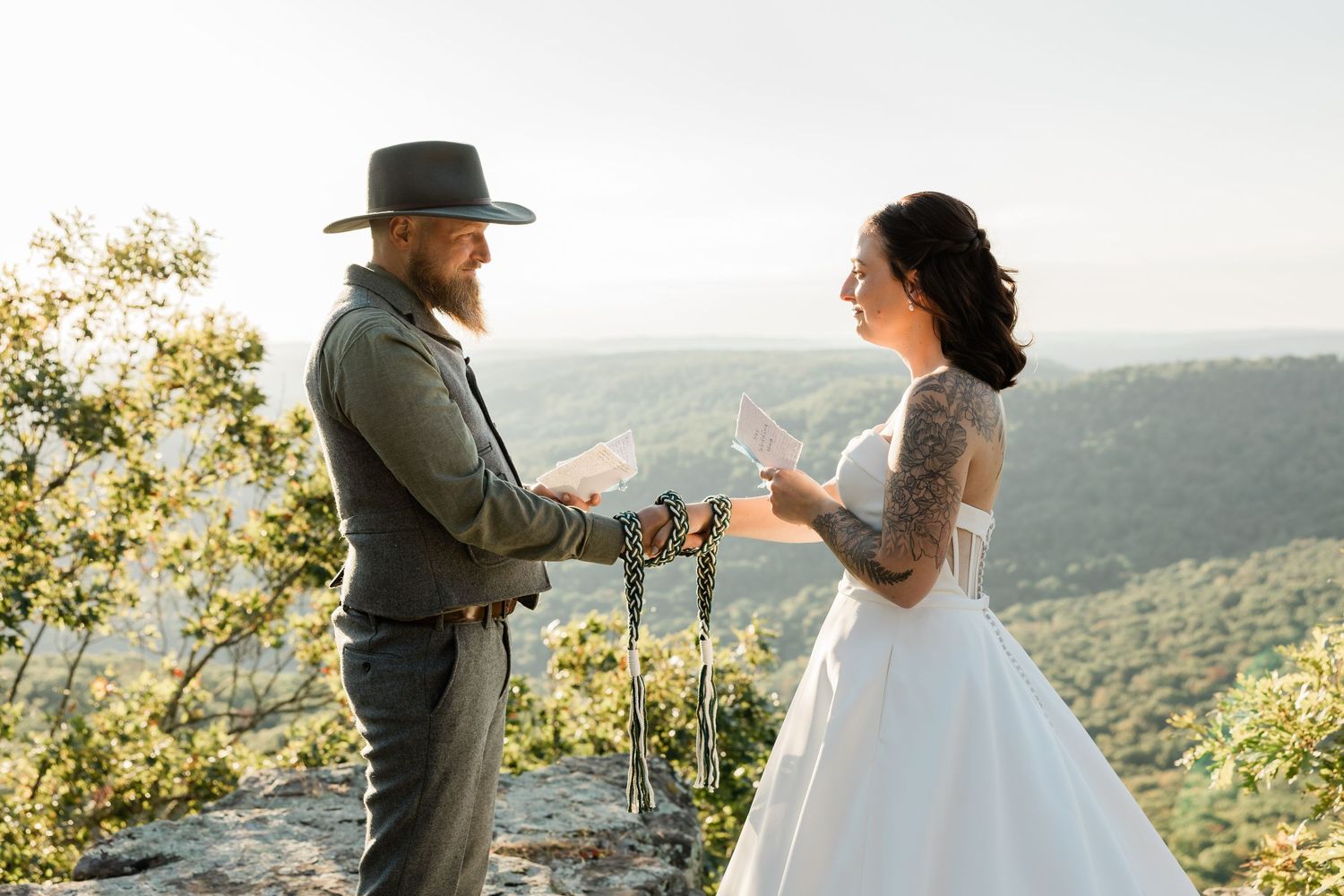 A couple exchanges vows during their mountaintop wedding ceremony with scenic valley views in the background.