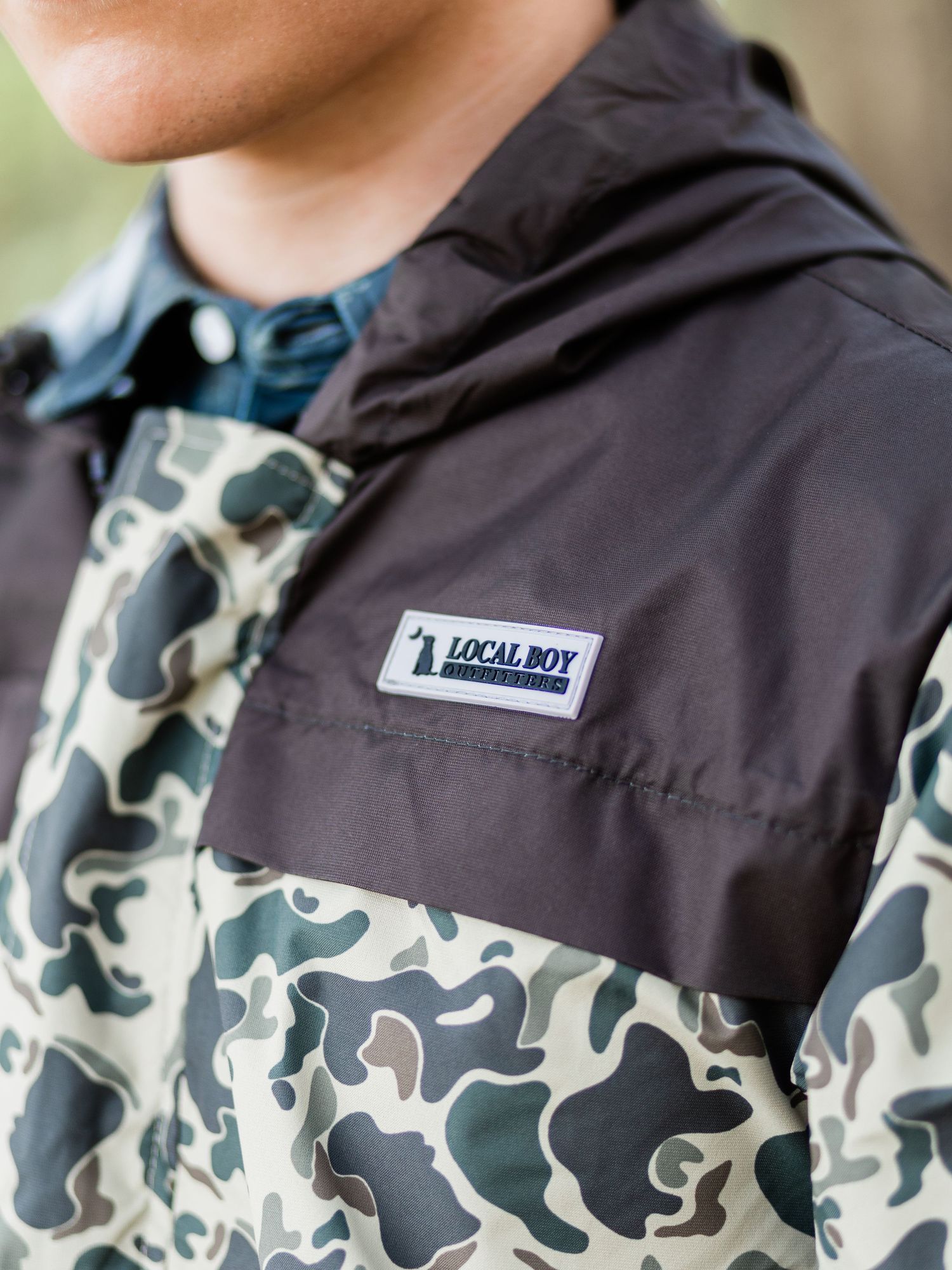 Man wearing a Local Boy Outfitters camo and black pullover hooded jacket with brand patch logo.