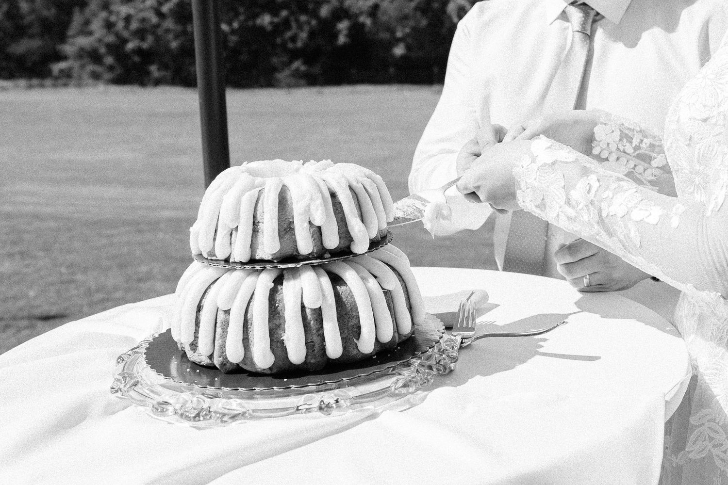 White bundt cakes arranged on a table with lace tablecloths at an outdoor event setting.