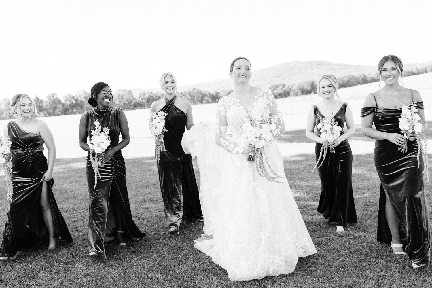 Wedding party poses playfully in black and white panoramic photo with bride in white dress and attendants in dark attire.