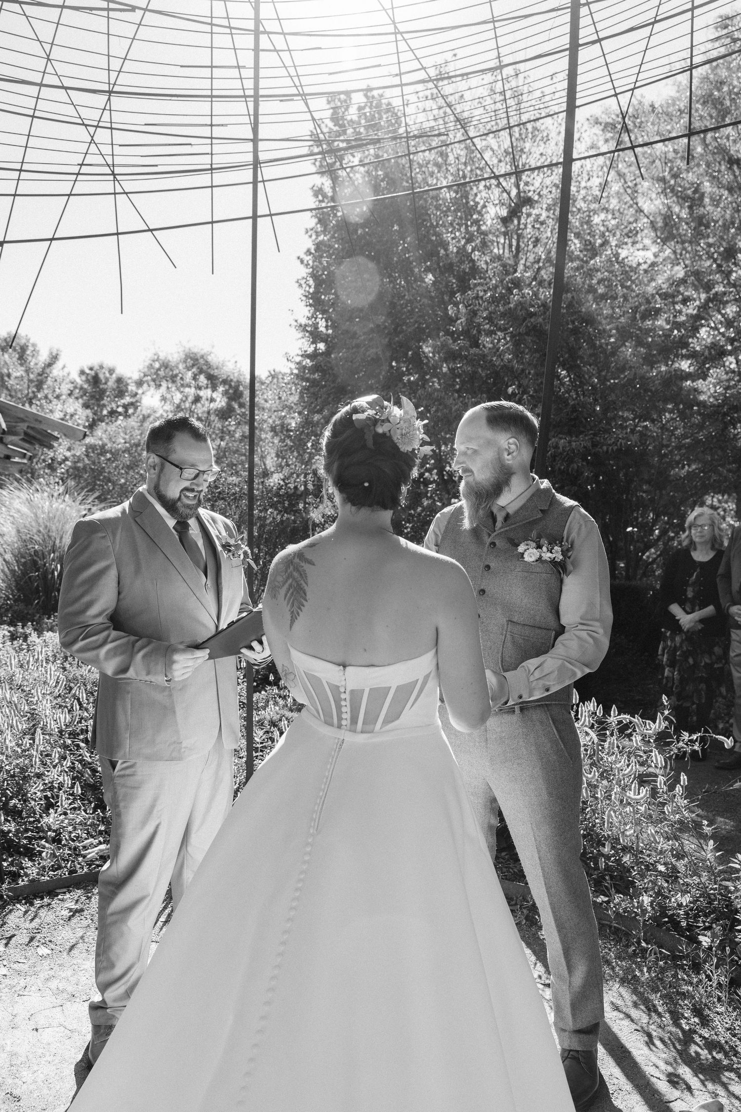 A wedding party poses together outdoors with the bride in a white gown and groomsmen in gray suits.