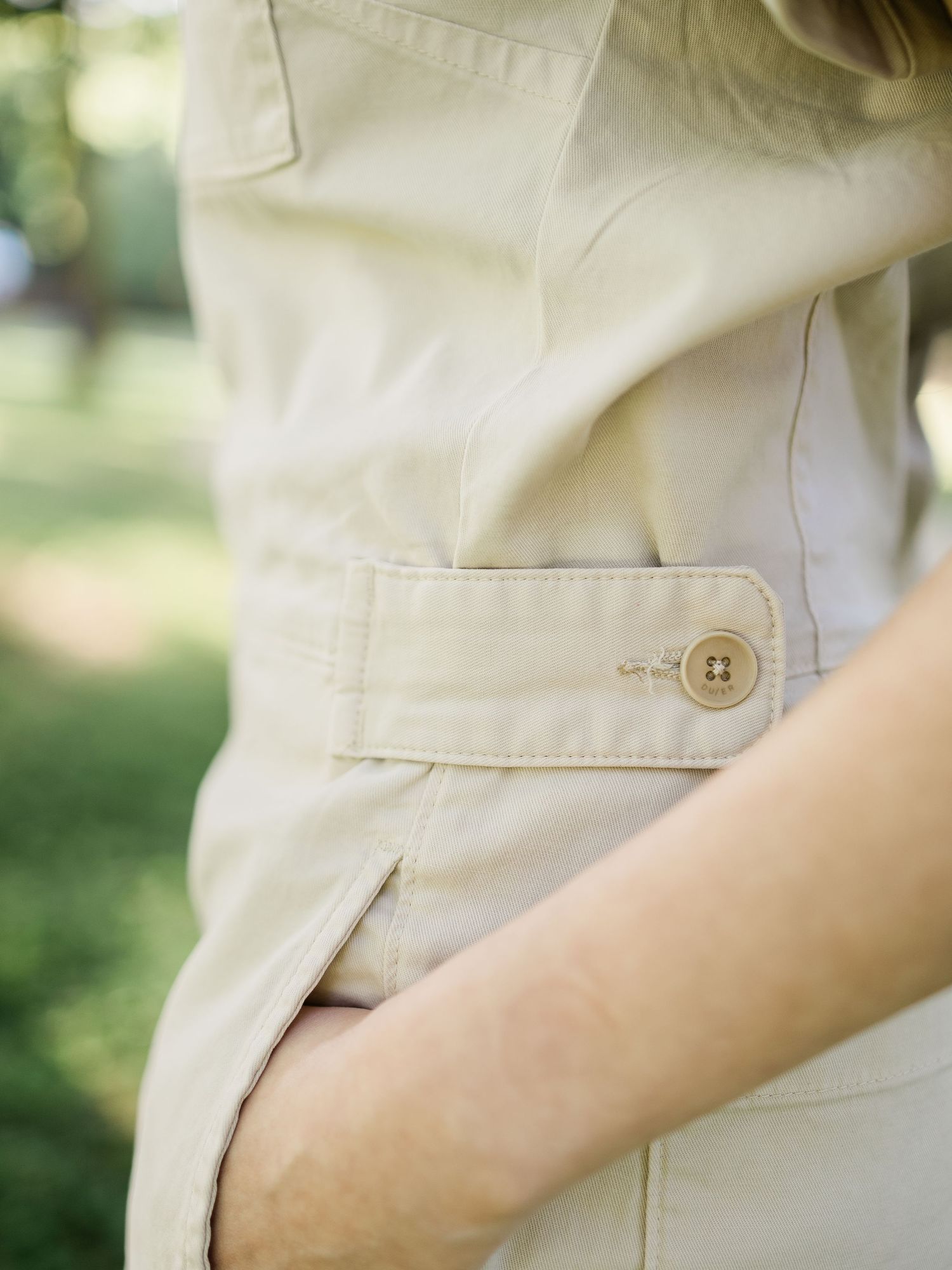Close-up of a beige cargo jacket with a button detail and belted waist, worn outdoors.