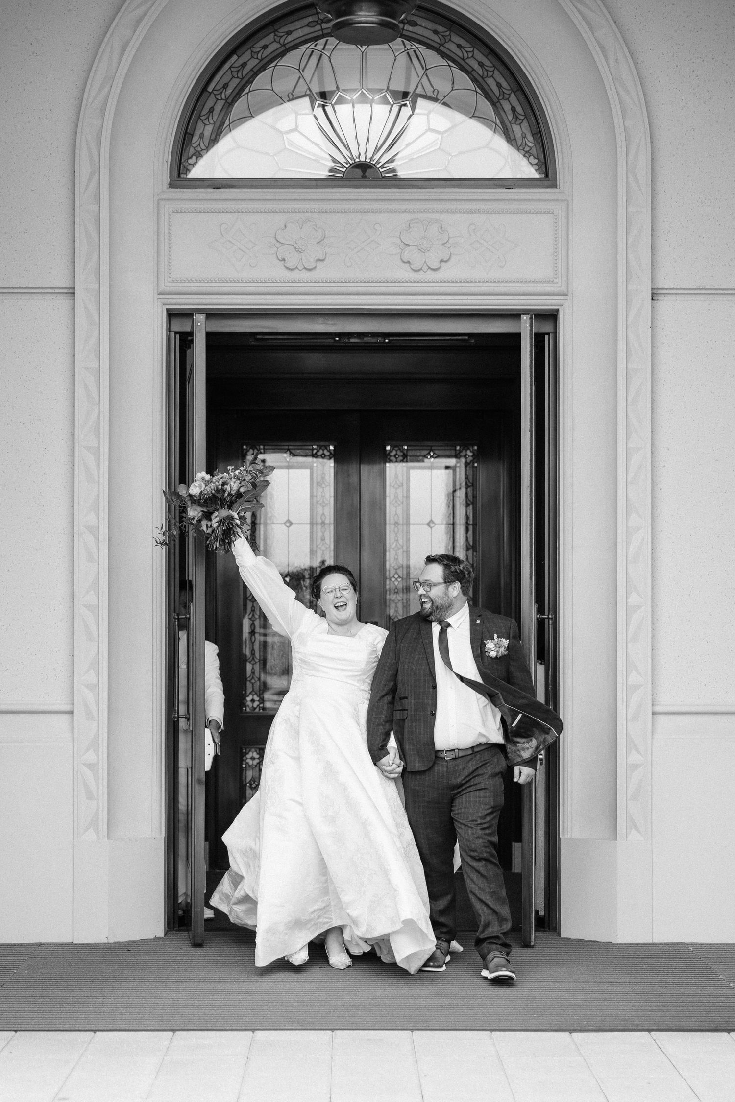 A joyful couple exits through an elegant arched doorway after their wedding ceremony.