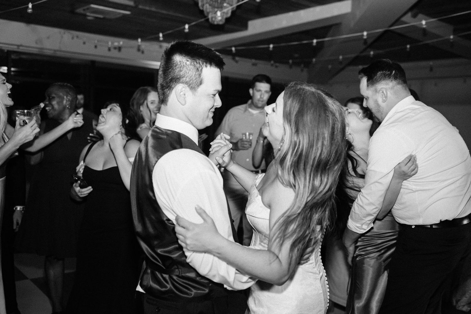 People dancing and socializing at what appears to be a wedding reception or party in black and white photography.