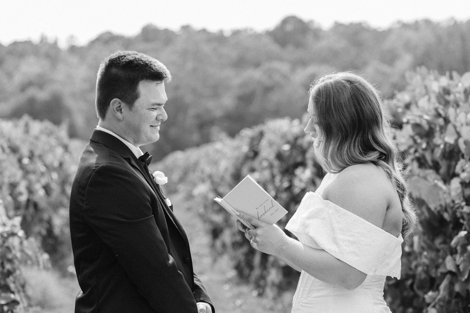 Black and white photo showing couple reading letters together in a scenic vineyard setting.