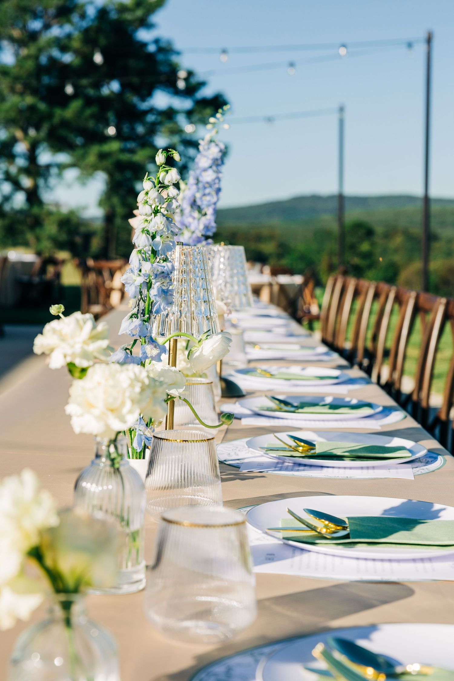 Elegant outdoor wedding reception table setting with white linens and glass vases in a scenic mountain venue.