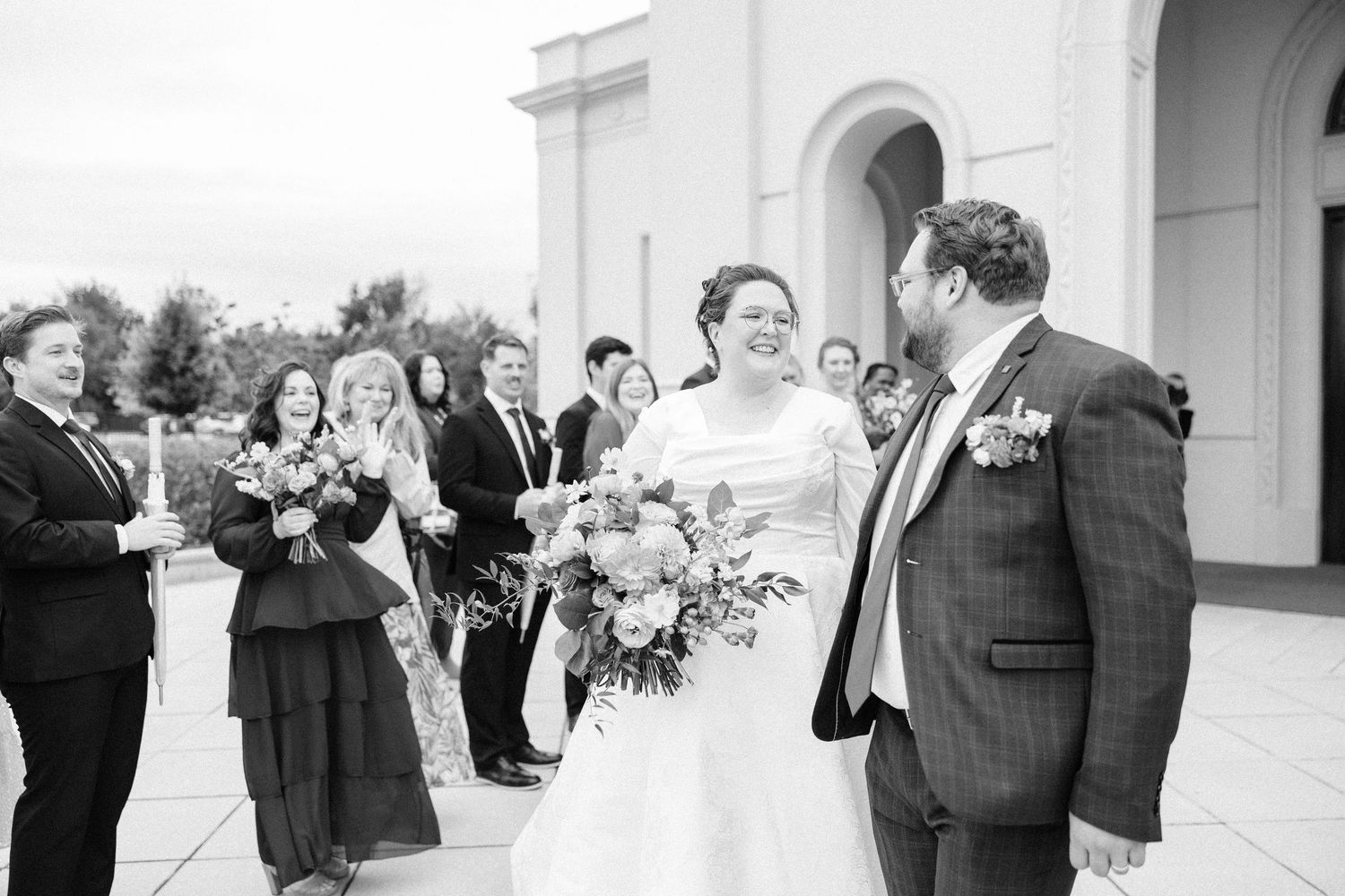 Wedding party celebrates with joyful laughter on the steps of a white columned building.
