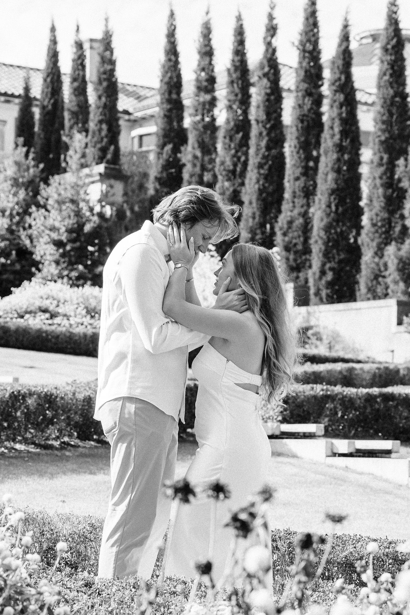 Black and white photo sequence of a couple dancing together in a garden with cypress trees in the background.