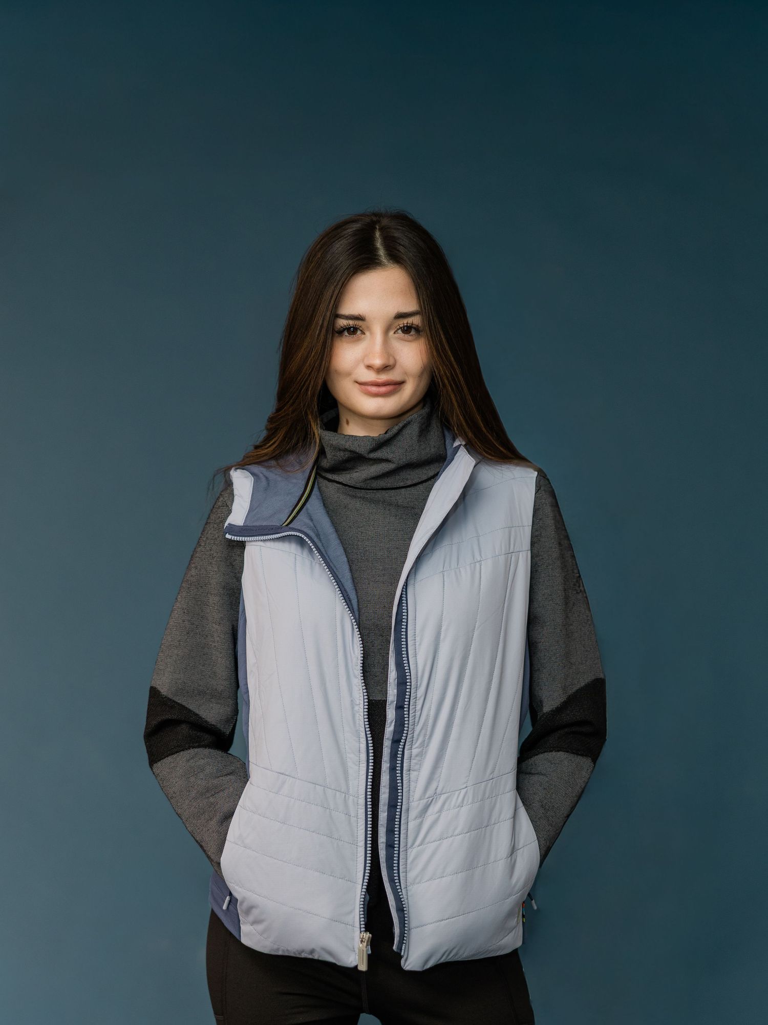 Model wearing a gray turtleneck sweater and light gray quilted vest against a dark background.