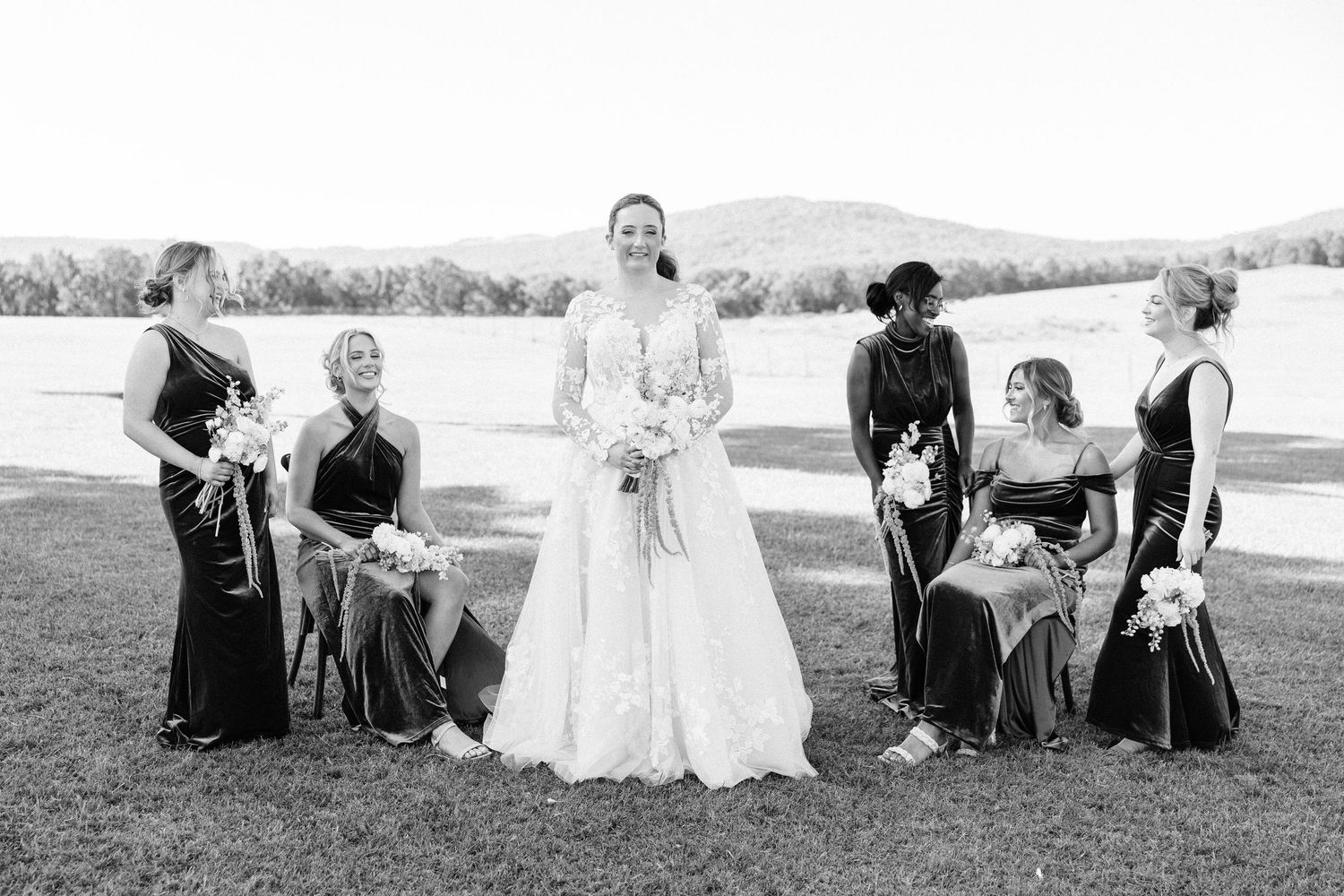 Wedding party posed outdoors on grassy field with mountains in background.
