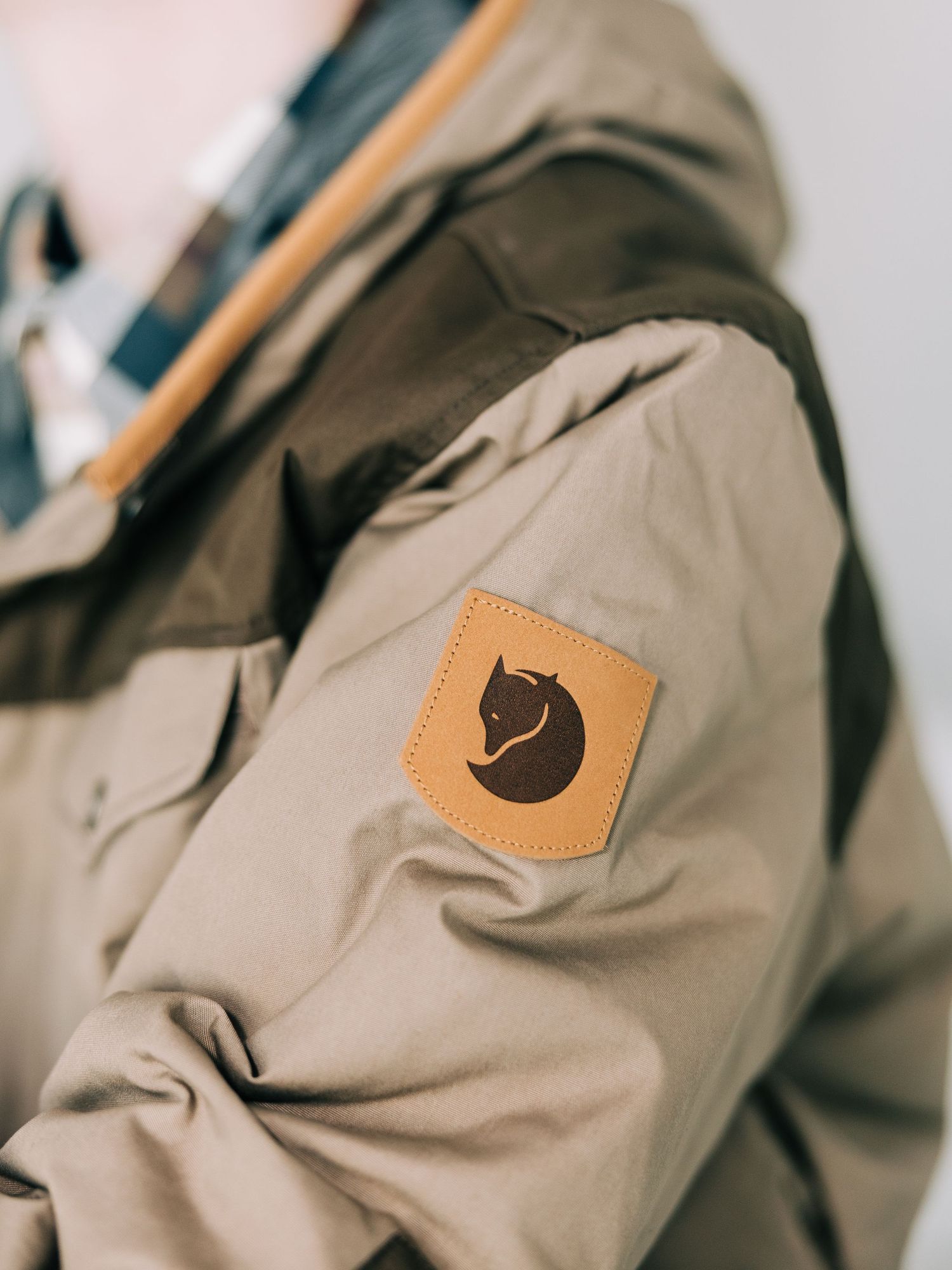 Close-up view of a tan Fjallraven backpack showing the brand's iconic fox logo patch detail on the shoulder strap.