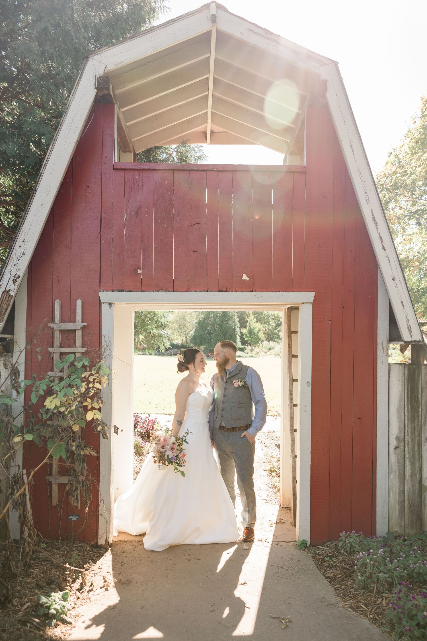 Wedding portraits taken in front of a rustic red barn with white trim and natural sunlight.
