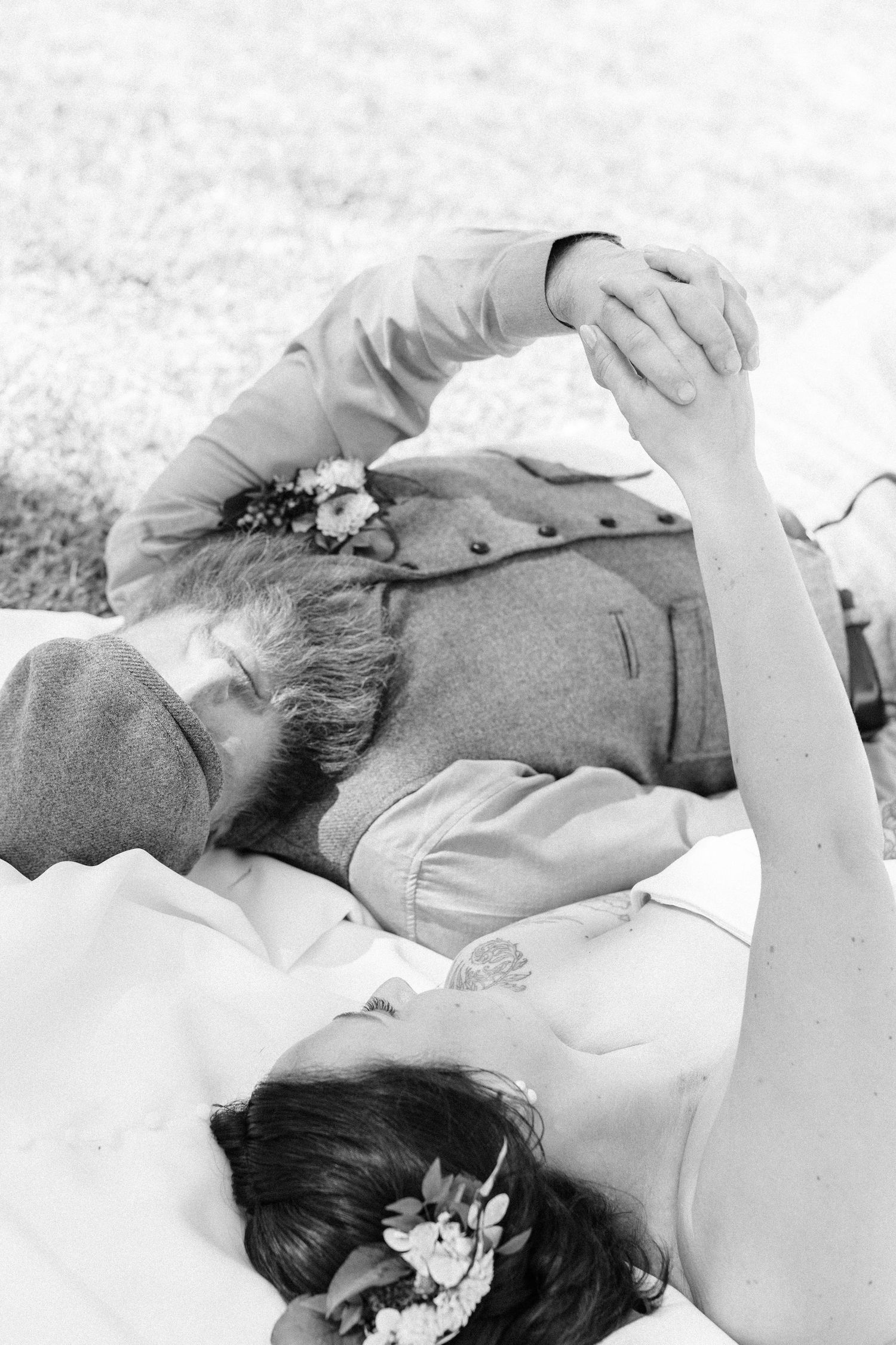 A romantic black and white portrait of a couple lying together with delicate flowers in their hair.