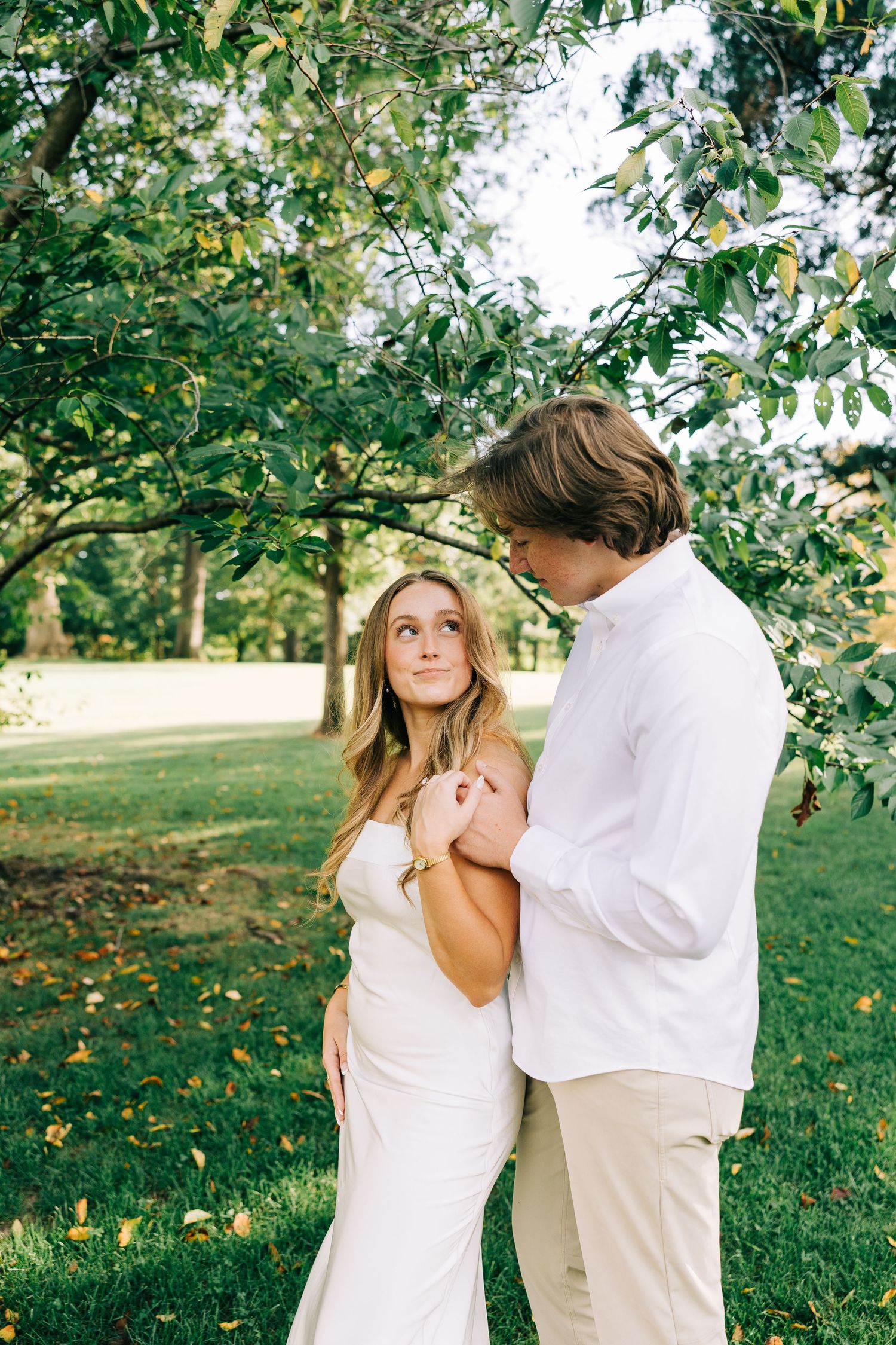 A romantic couple in white outfits share tender moments in a sun-dappled apple orchard during a photo session.