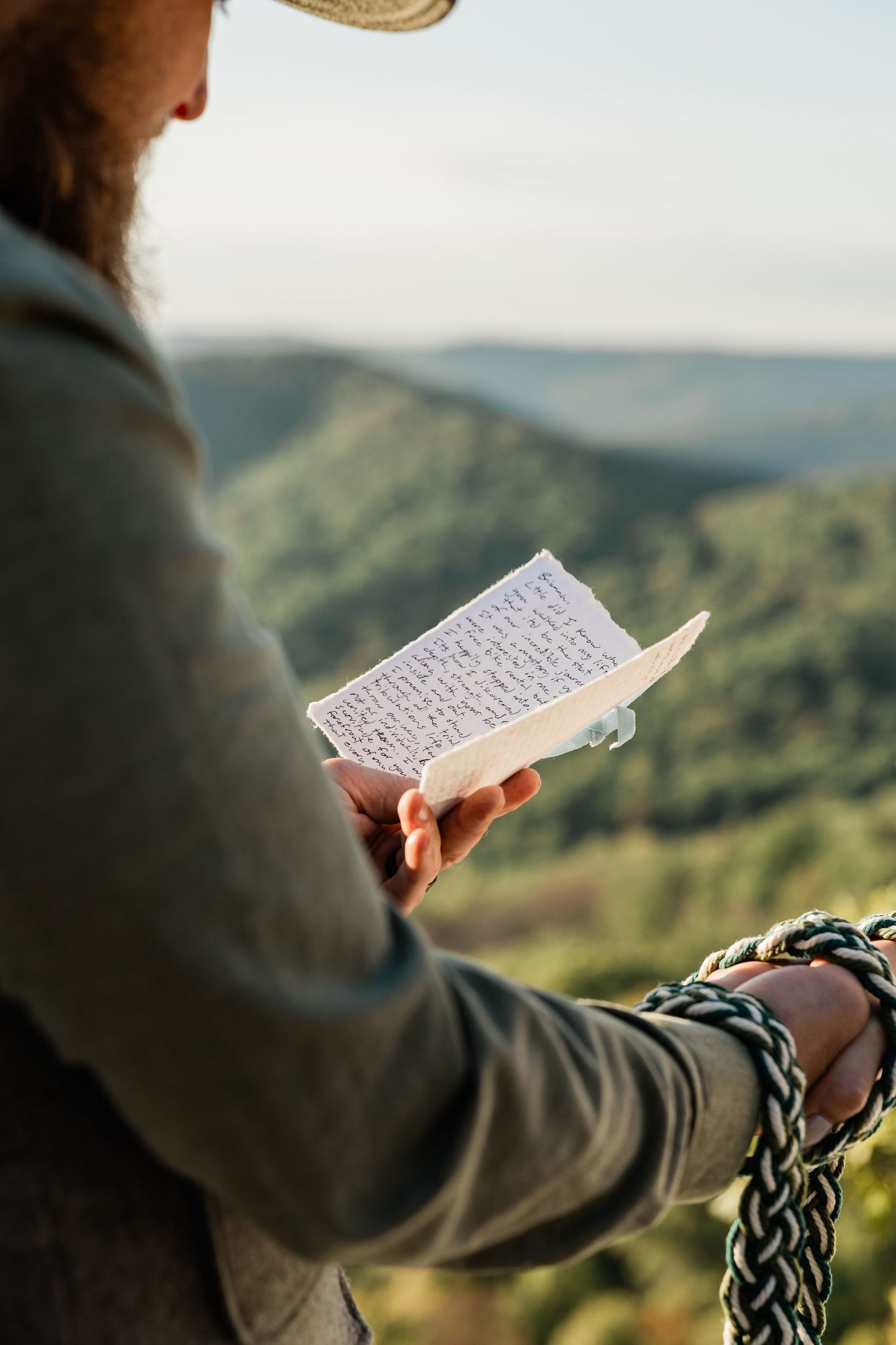 Reading handwritten vows against scenic mountain backdrop during outdoor wedding ceremony.