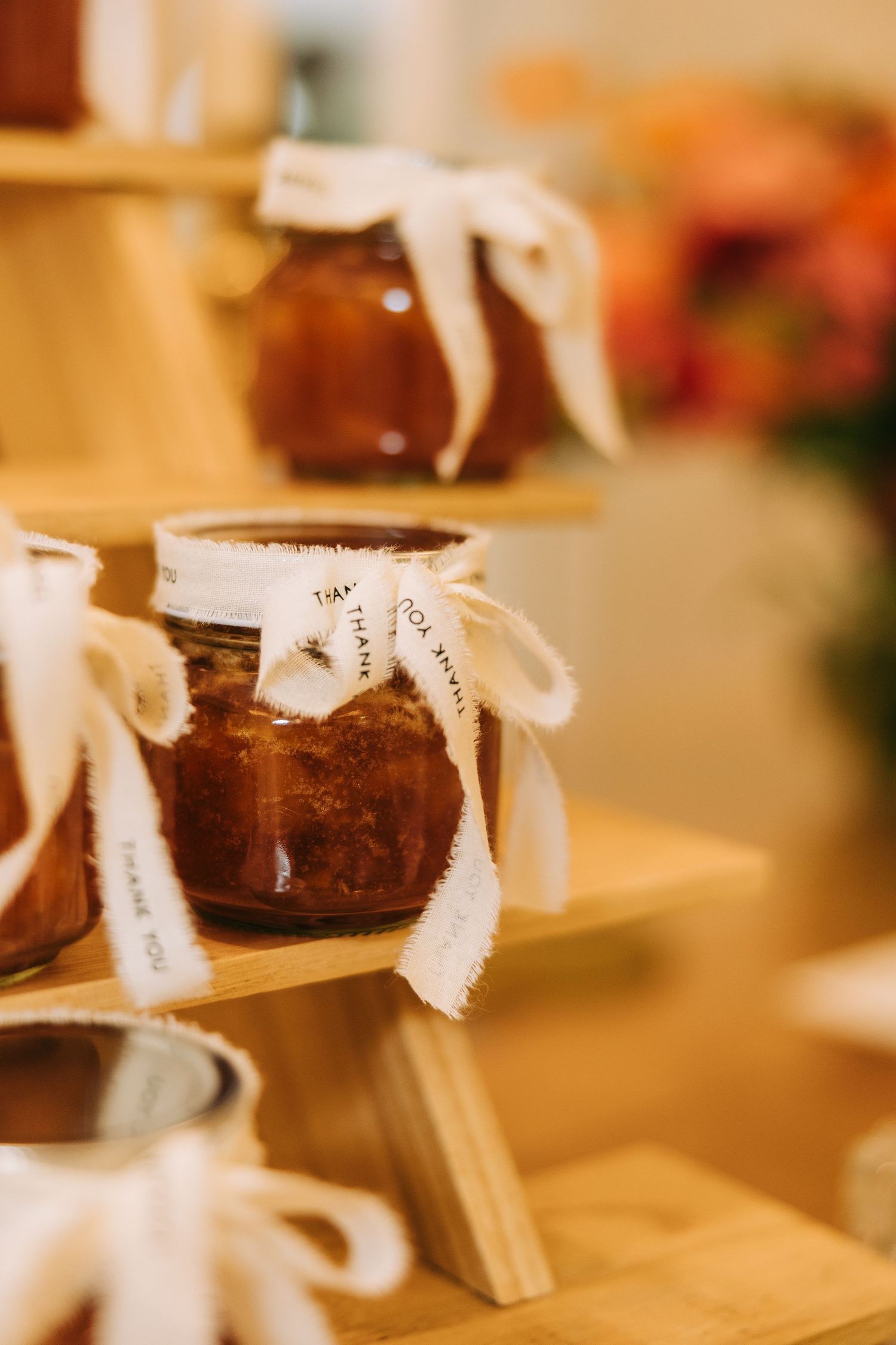 Small glass jars with white ribbon bows displayed as wedding favors on wooden surface.