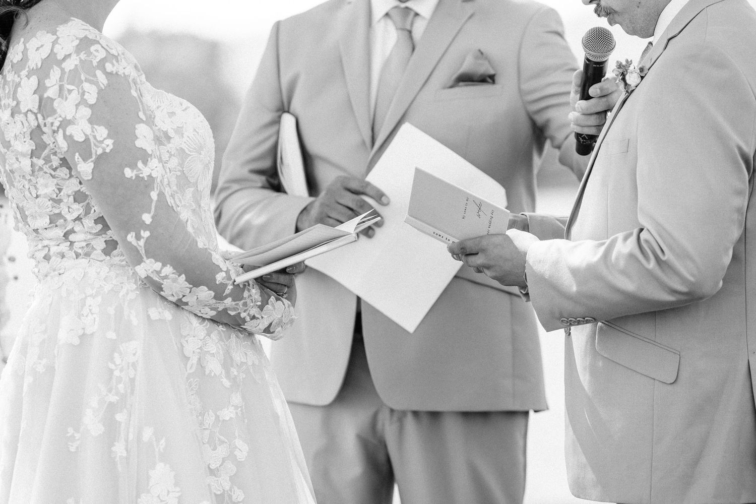Wedding party in light colored attire stands together during outdoor ceremony.