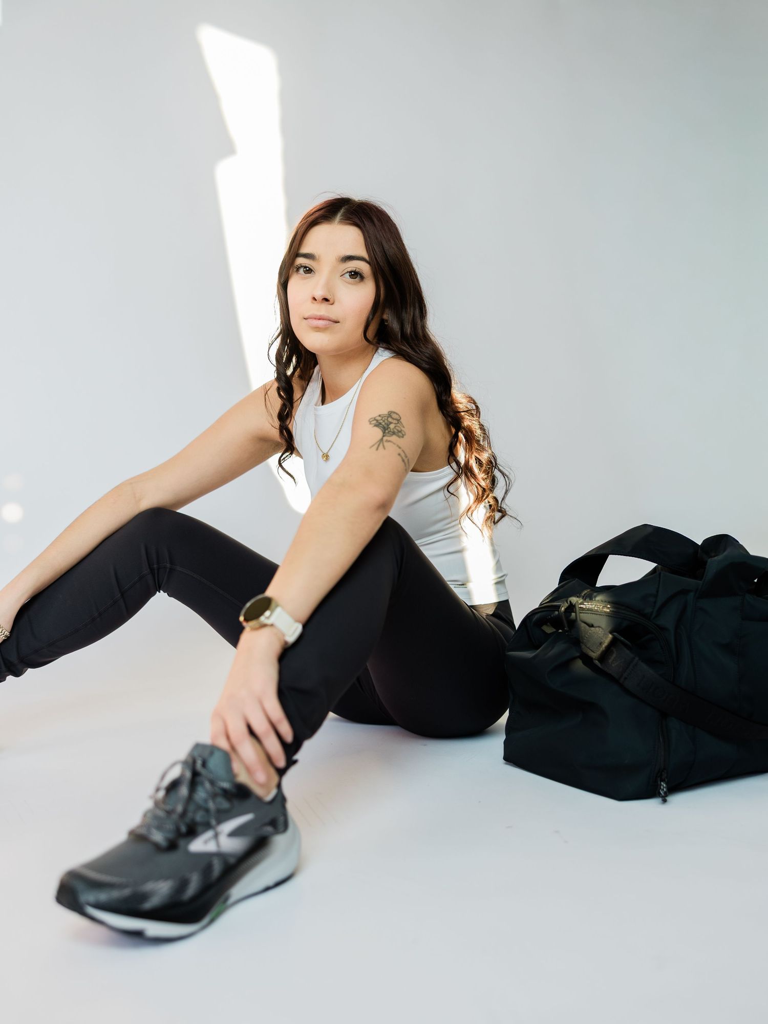 A person in black attire lies on a white floor wearing black sneakers, creating a minimalist fashion aesthetic.