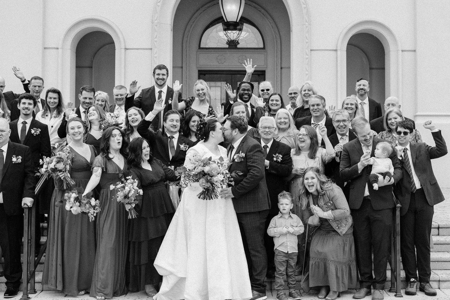 Panoramic view of wedding guests and bridal party assembled on classic white architectural steps.