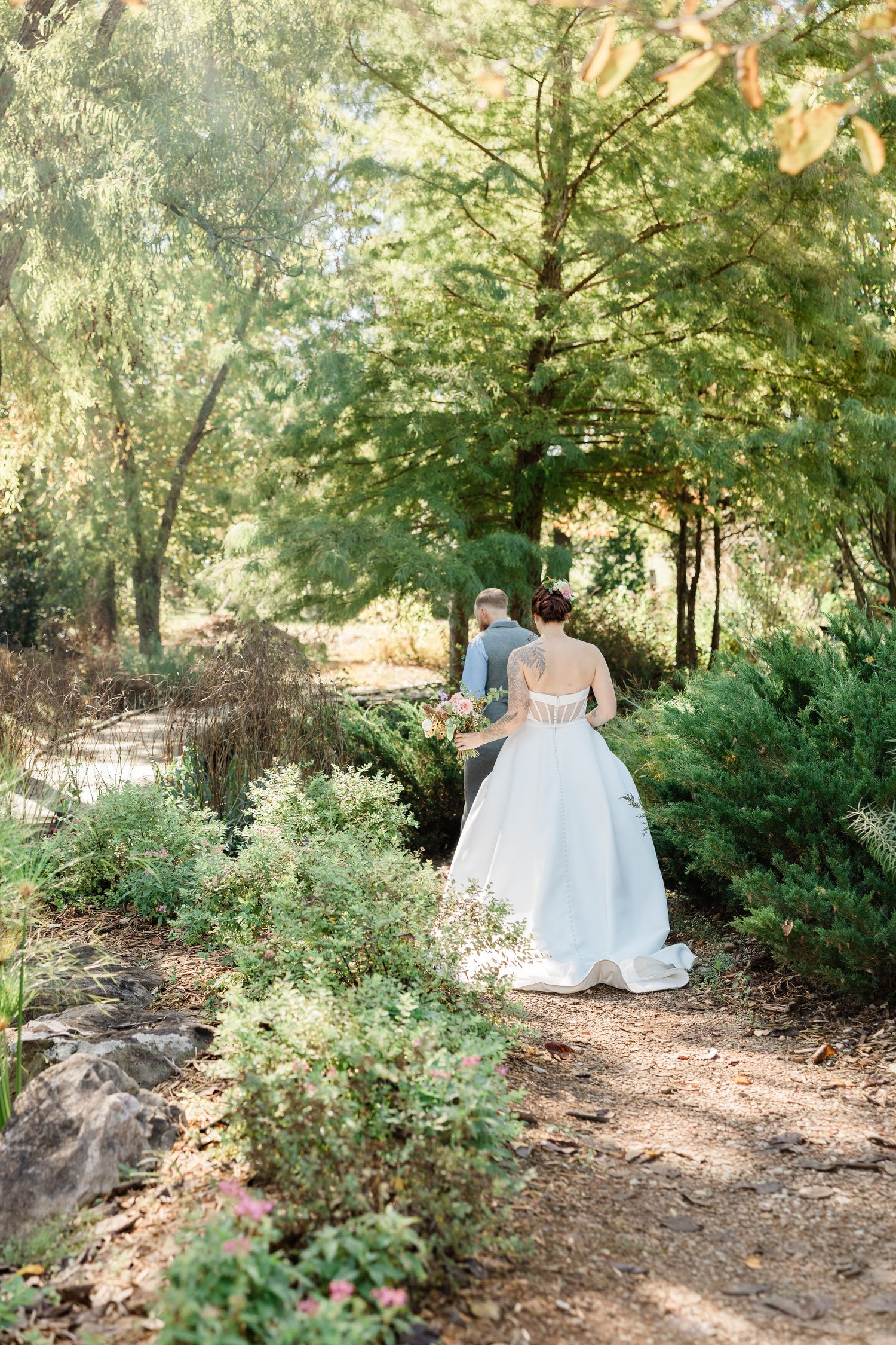 A couple walks hand in hand through a lush garden path on their wedding day.