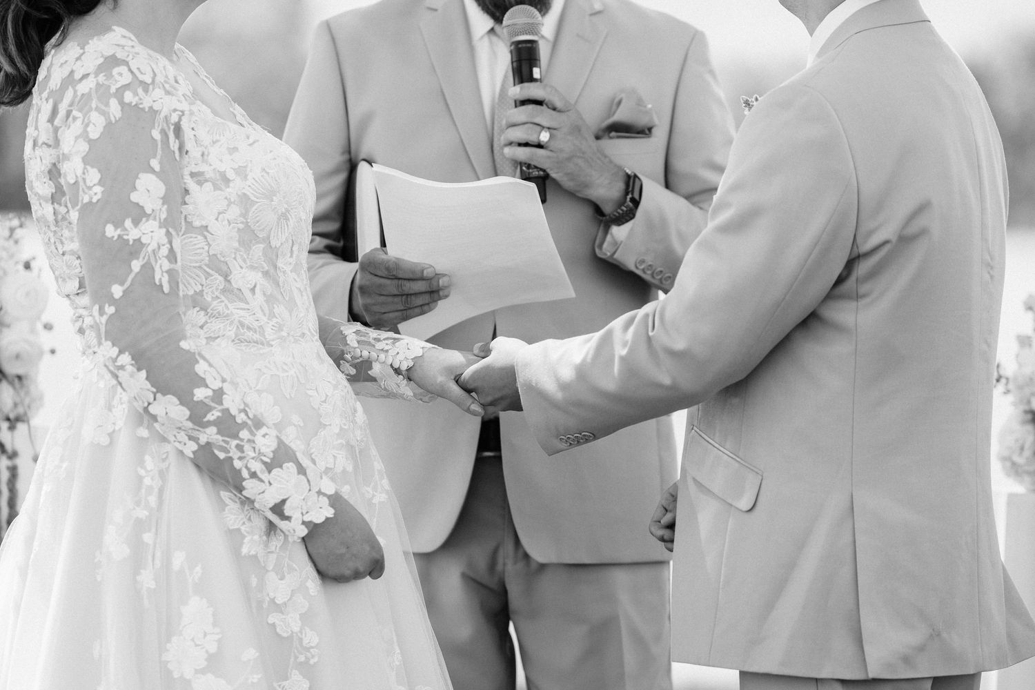 Wedding ceremony participants in light colored attire standing together outdoors.