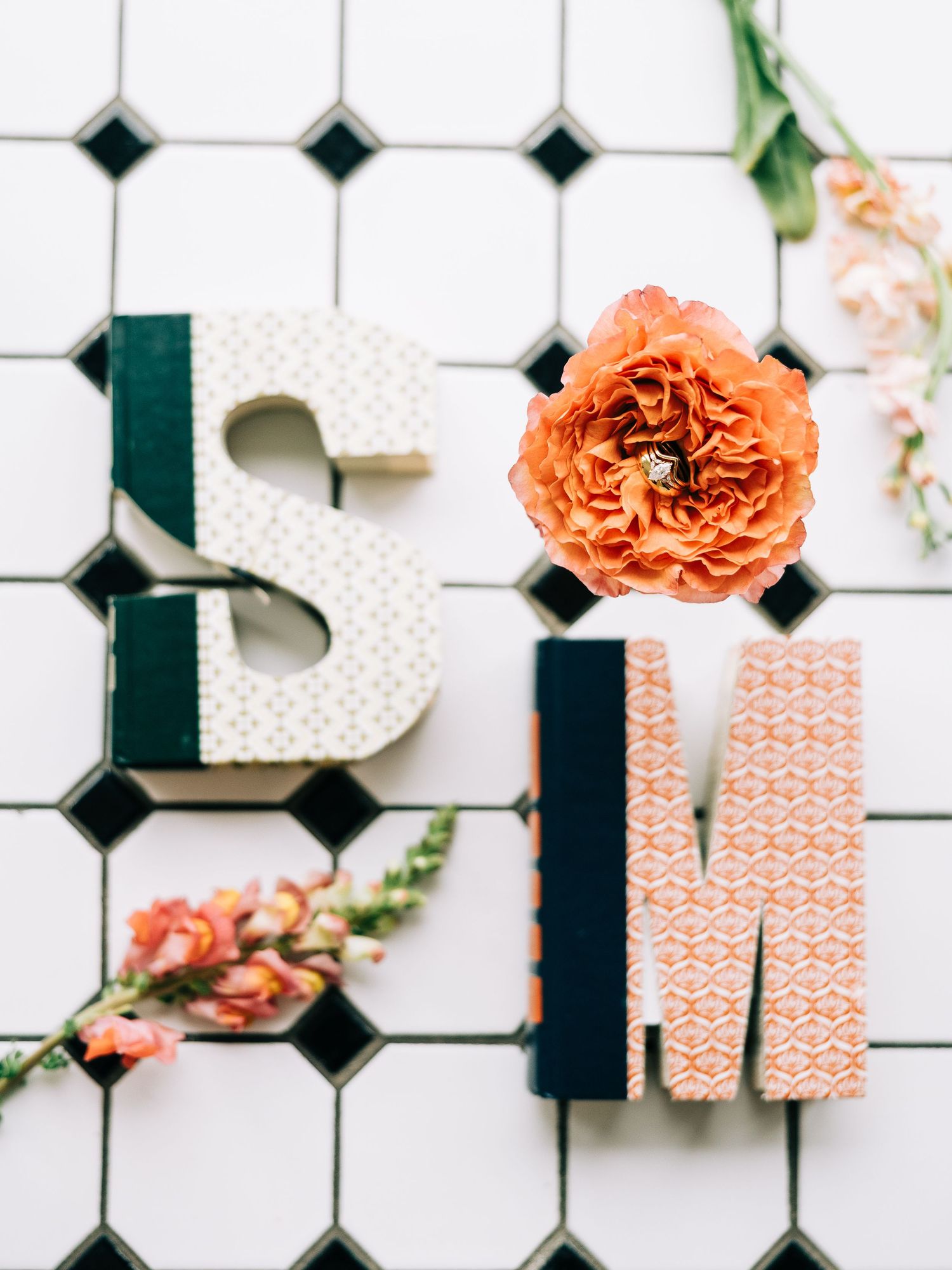 Decorative letters 'B' and 'M' with coral flowers on white tile background.