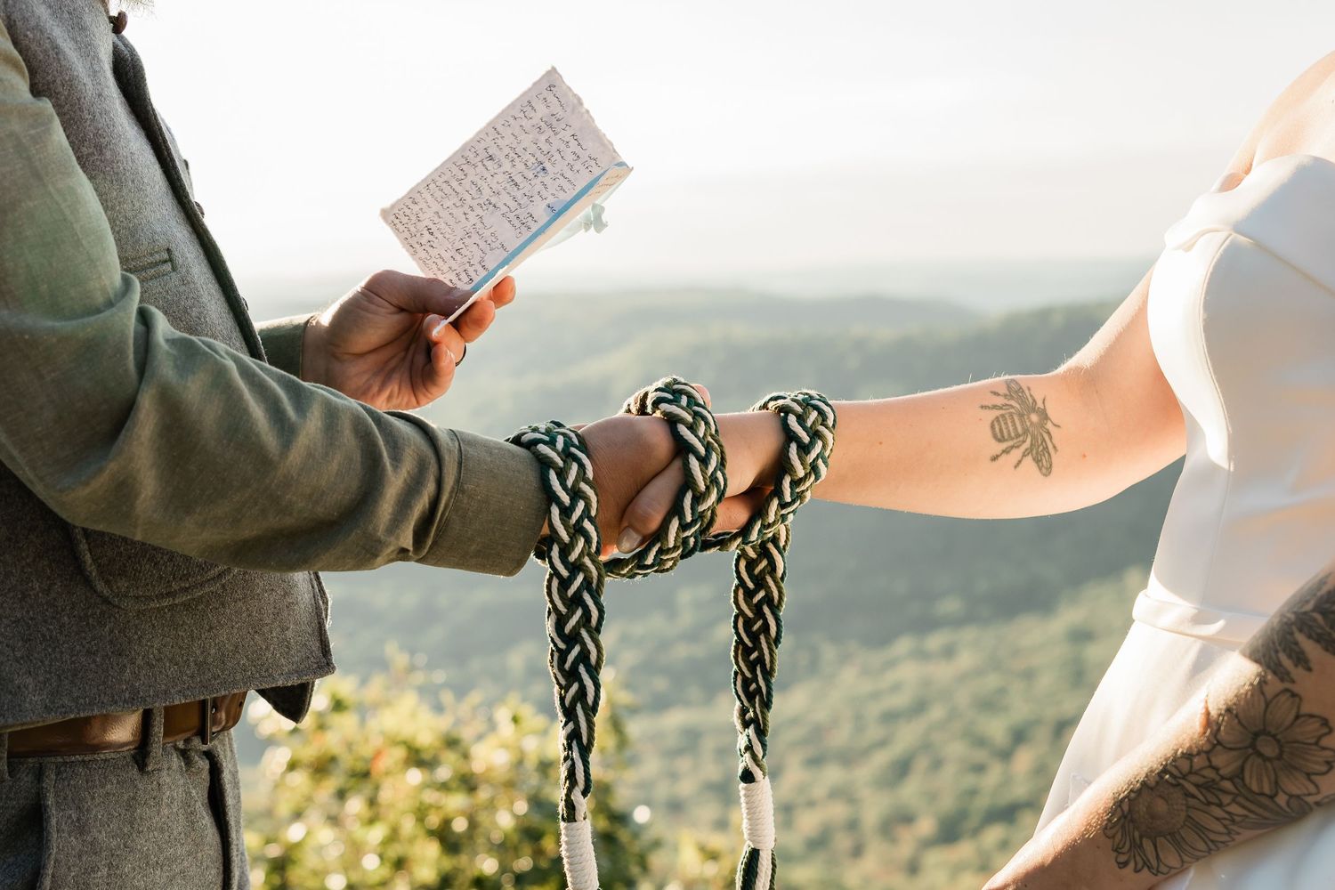 Couple holding handwritten vows with mountain landscape in background at sunset.