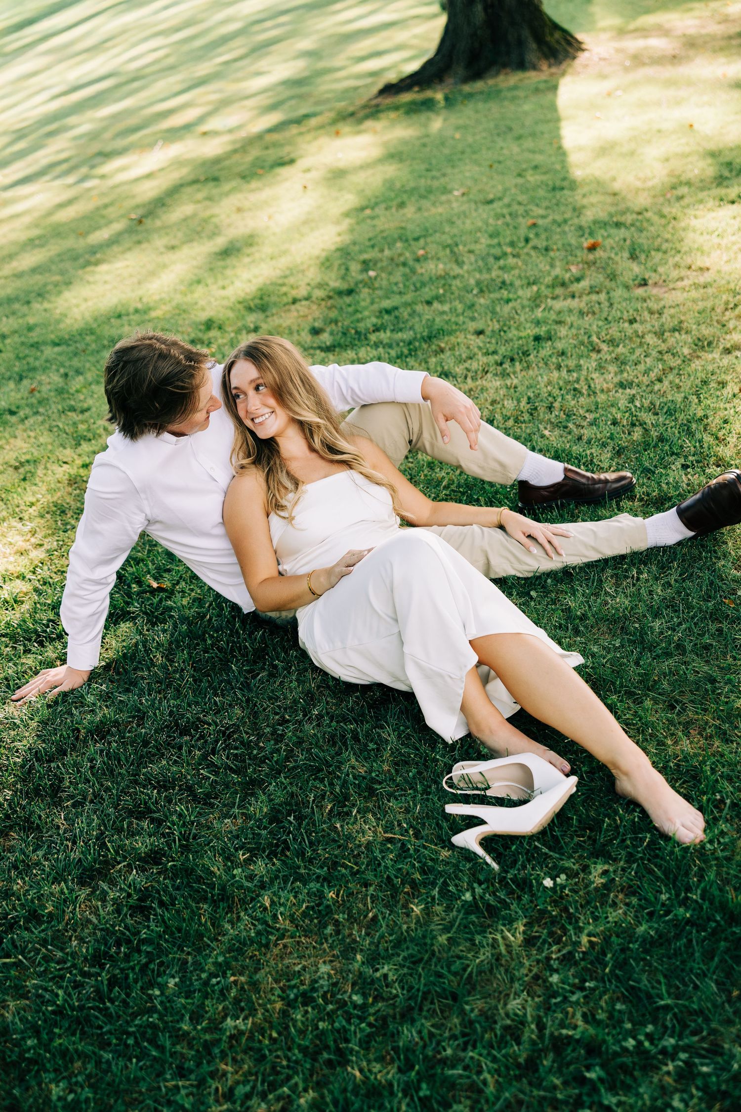 A couple in white clothing lies together on green grass in a romantic outdoor setting.