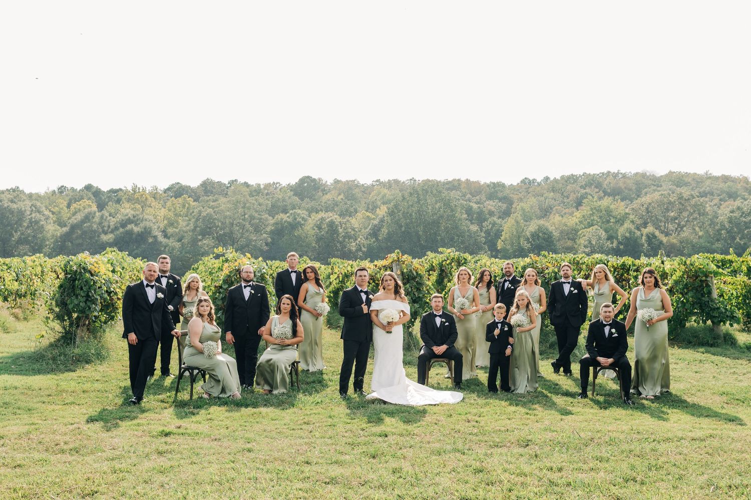 A wedding party poses together in a scenic outdoor field with trees in the background.