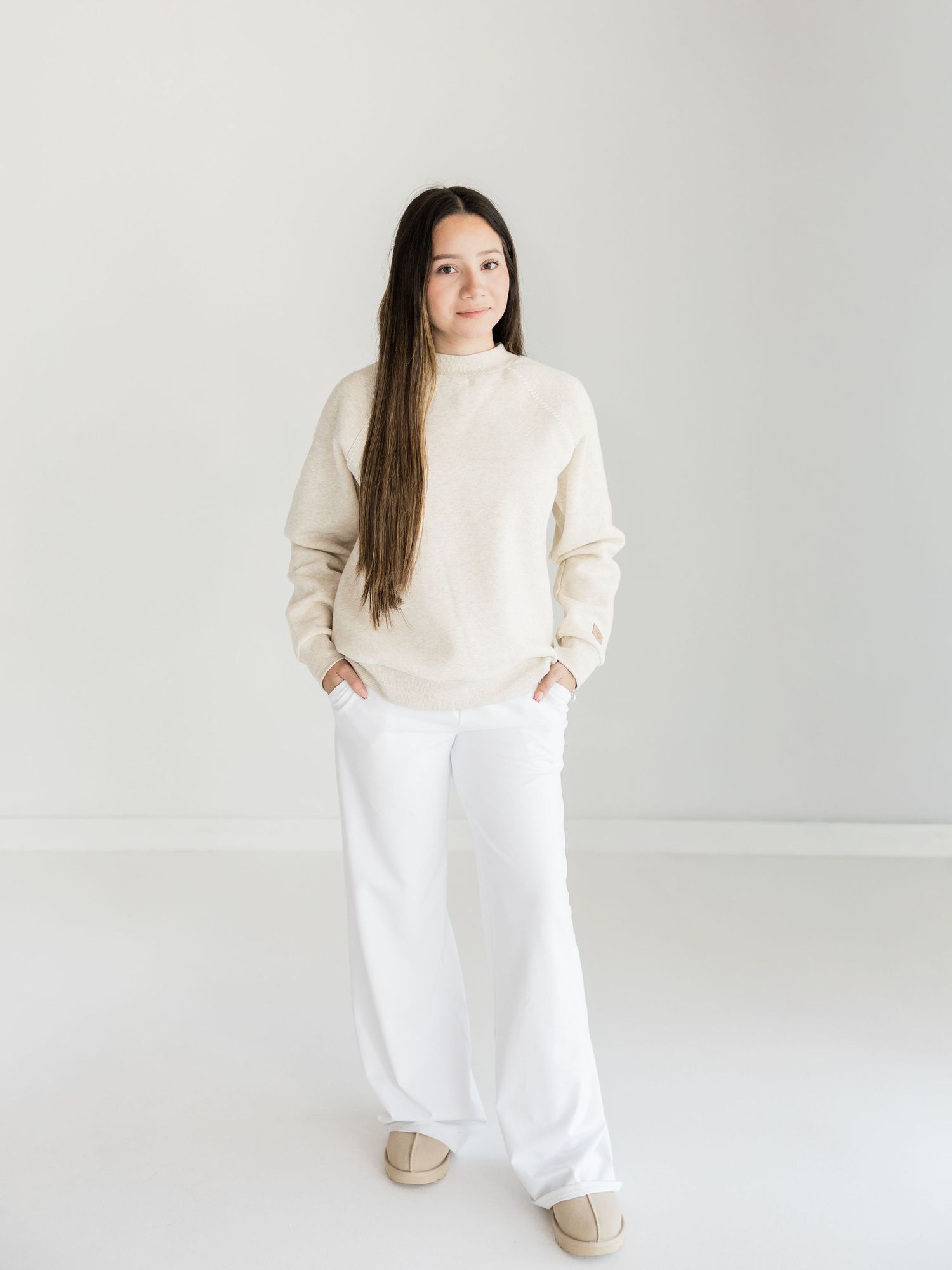 Woman wearing a cream mock neck sweater and wide-leg white pants with beige slip-on shoes.