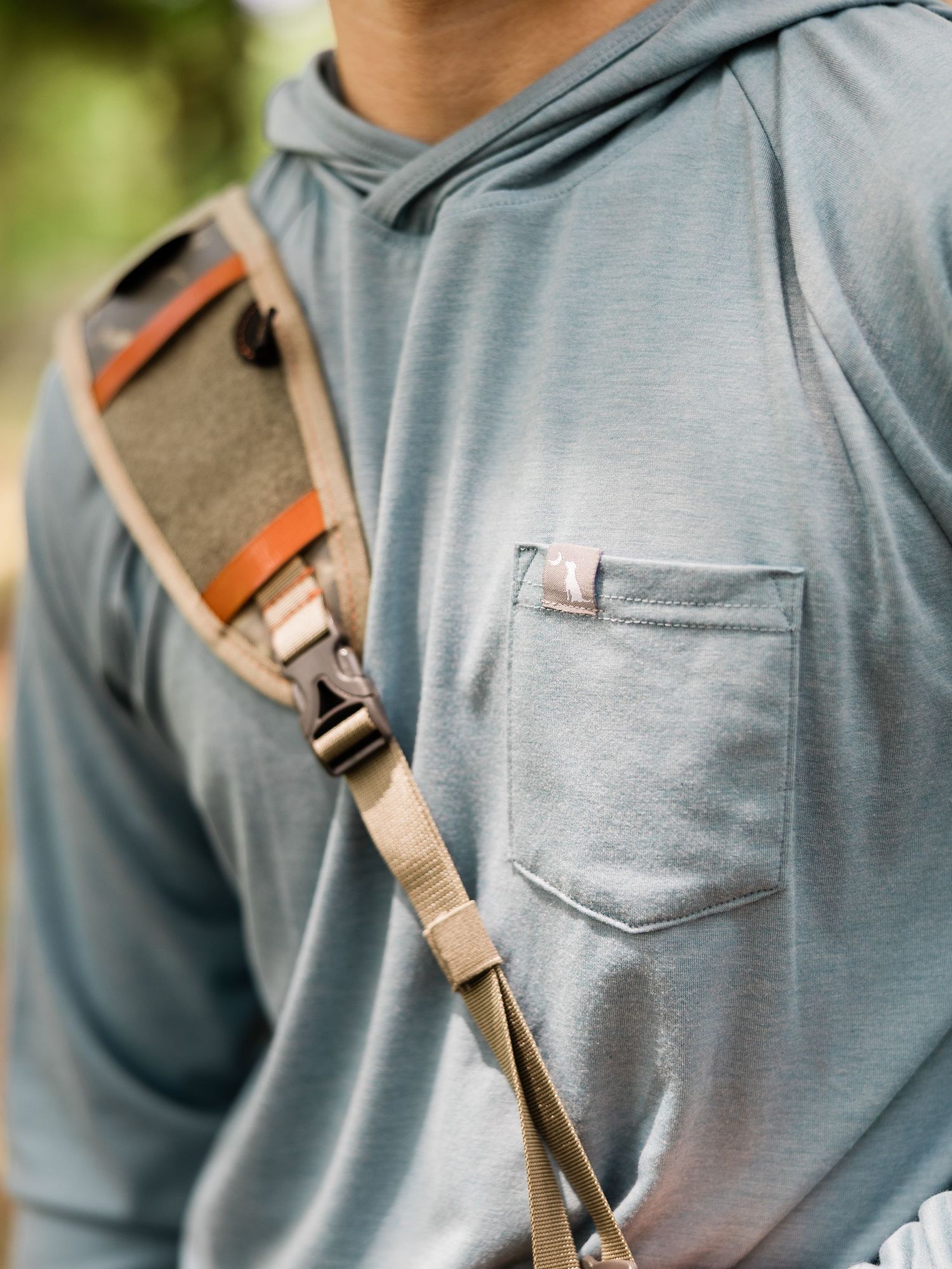 Person wearing a gray hoodie with a tan canvas crossbody bag strap across their chest outdoors.