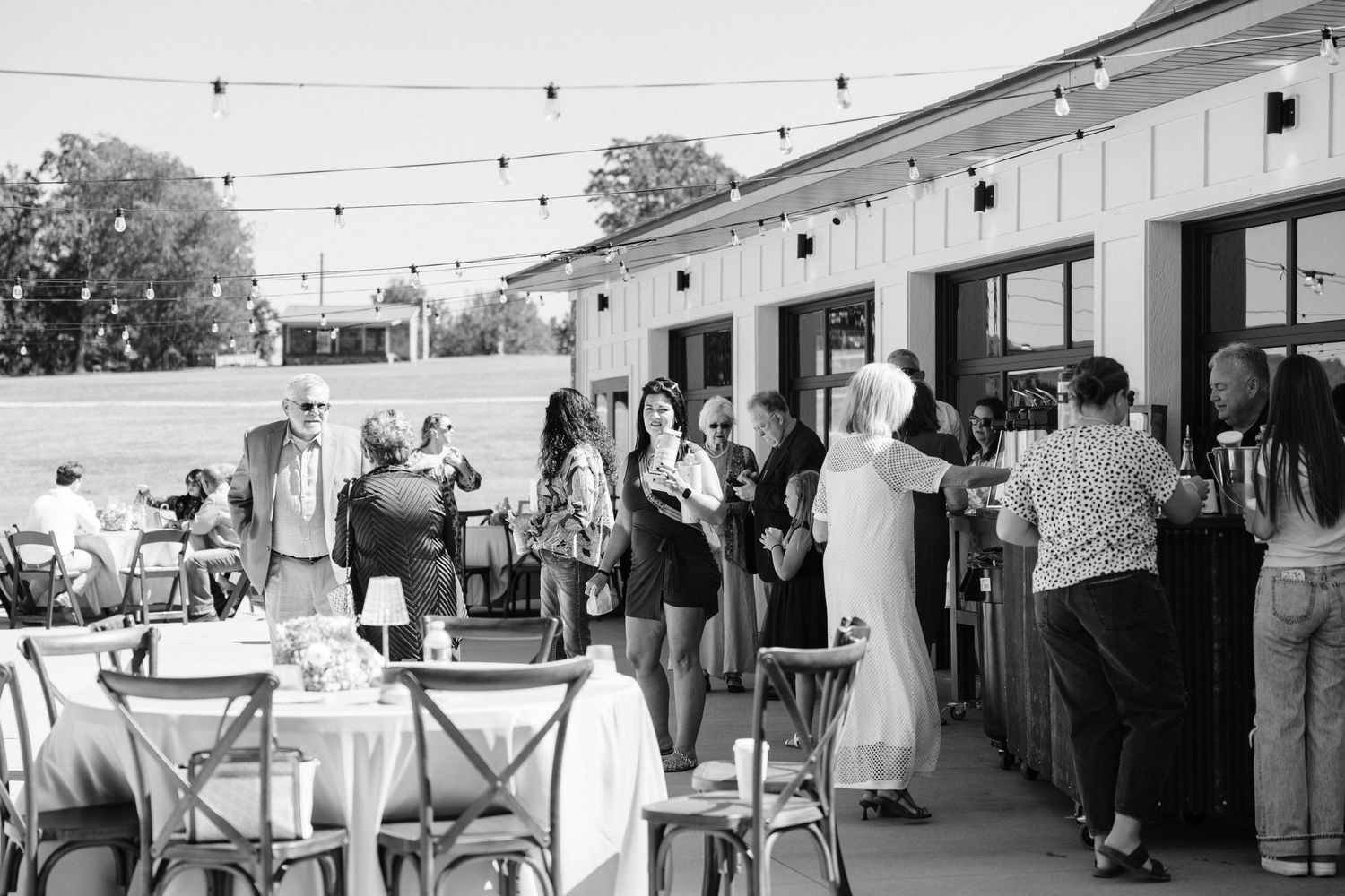 Black and white photo of wedding reception guests mingling under string lights.