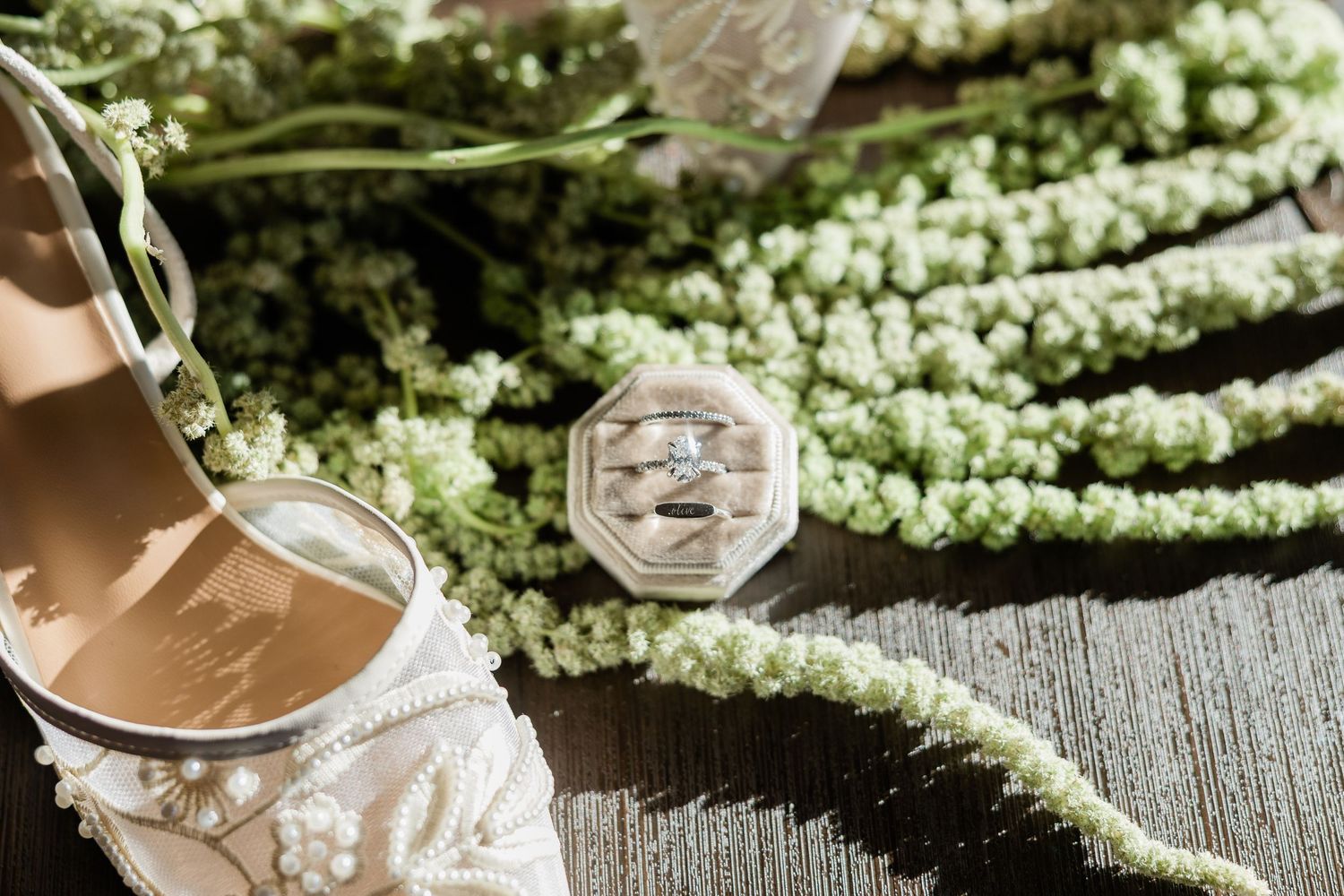 Wedding details including a ring box and delicate white floral arrangements on a rustic wooden surface.