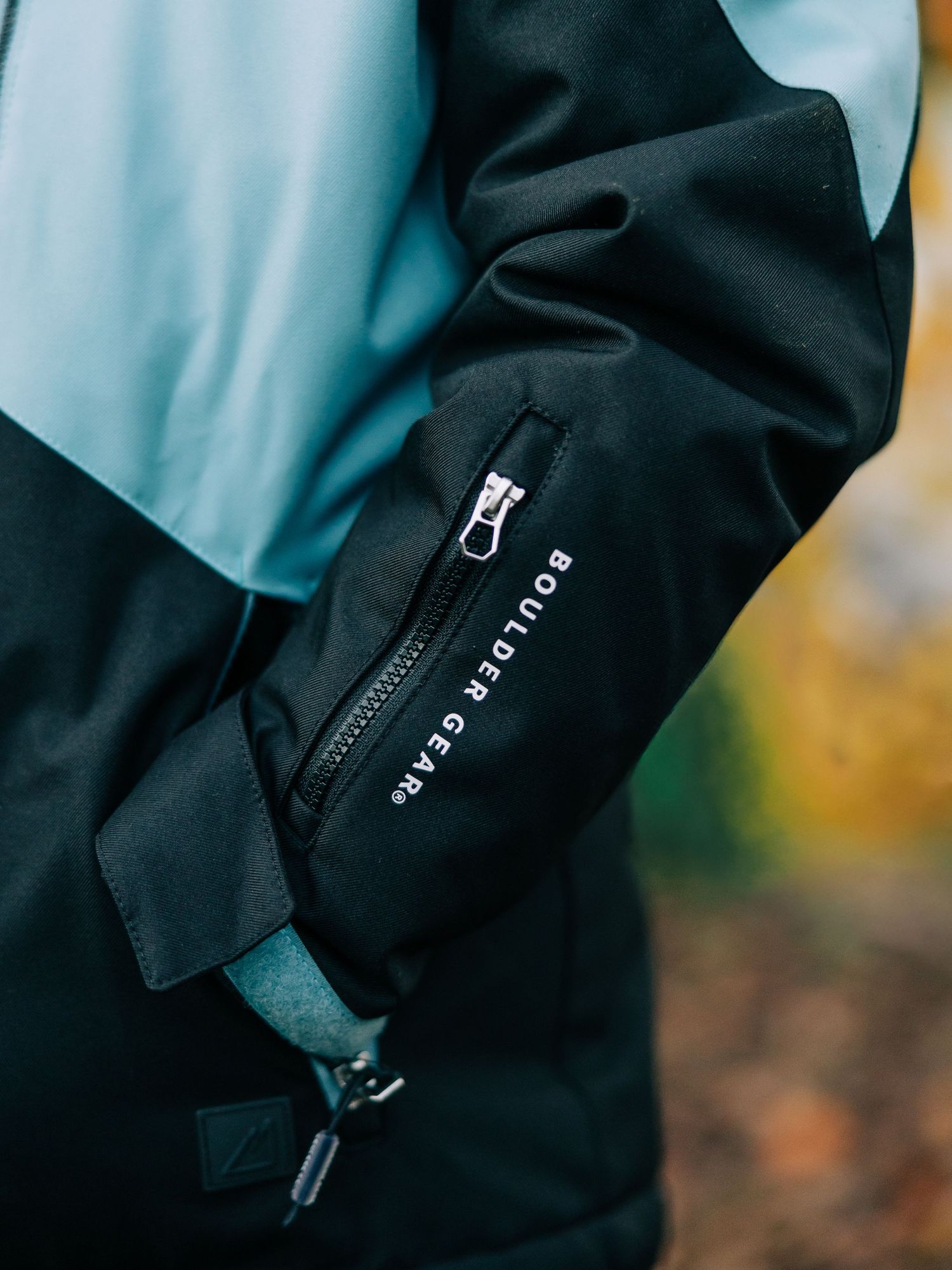 Close-up details of black technical outerwear showing zipper and fabric textures in a moody outdoor setting.