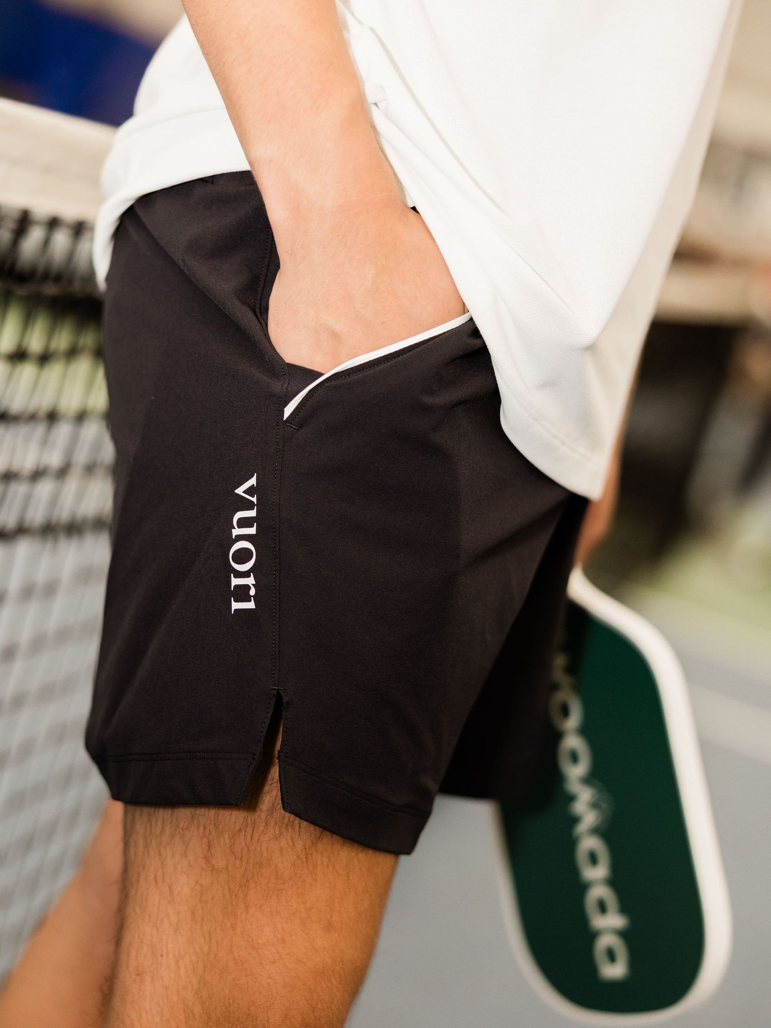 Man wearing black Vuori shorts holding a pickleball paddle on a court near the net.