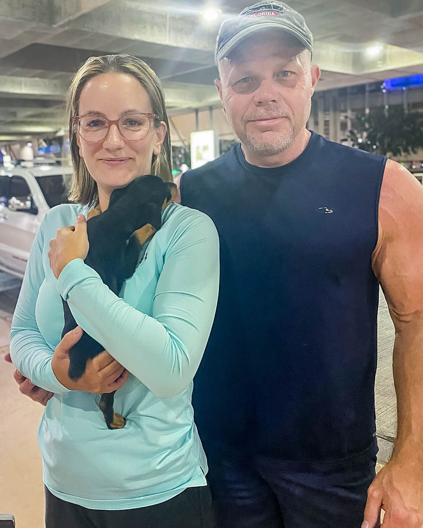 Couple smiling outdoors holding a small black Dachshund puppy at night after pet transport