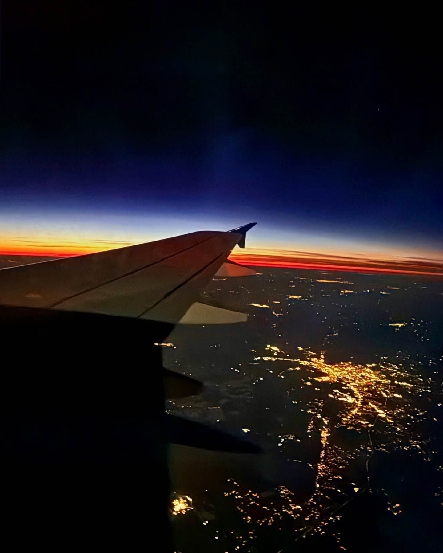 Stunning aerial view of city lights at dusk from airplane window with colorful horizon while doing a flight nanny service.