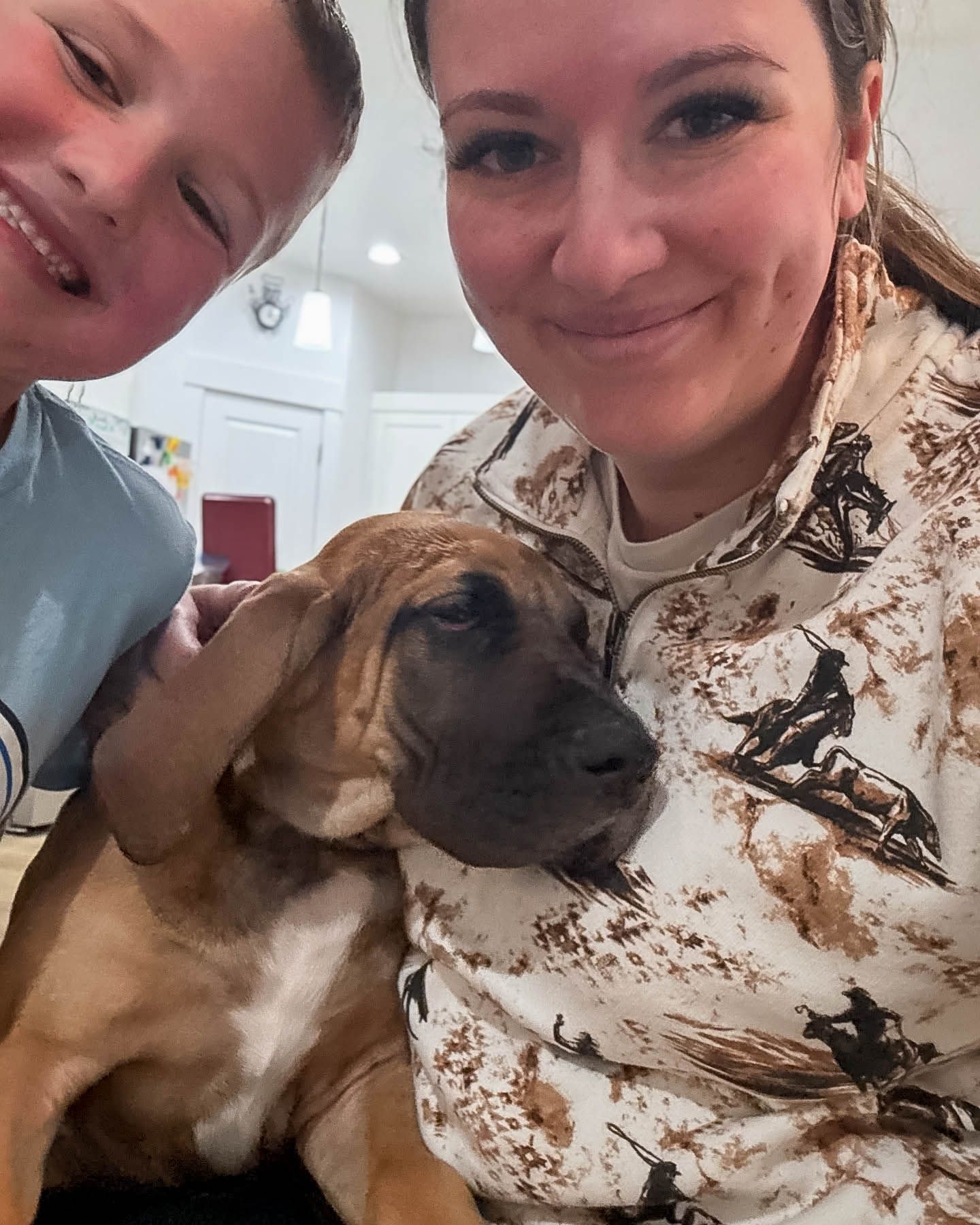 Woman and young boy taking a selfie with a brindle Mastiff puppy indoors.