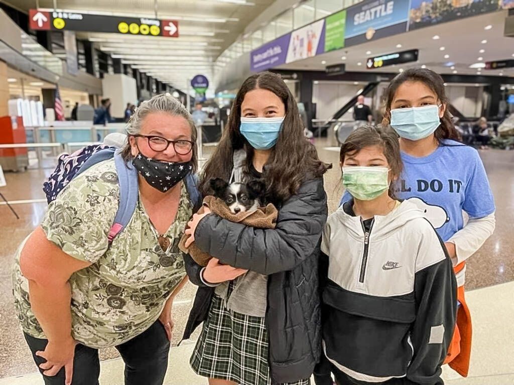 Family of four wearing masks at Seattle airport, child holding a small black and white puppy.