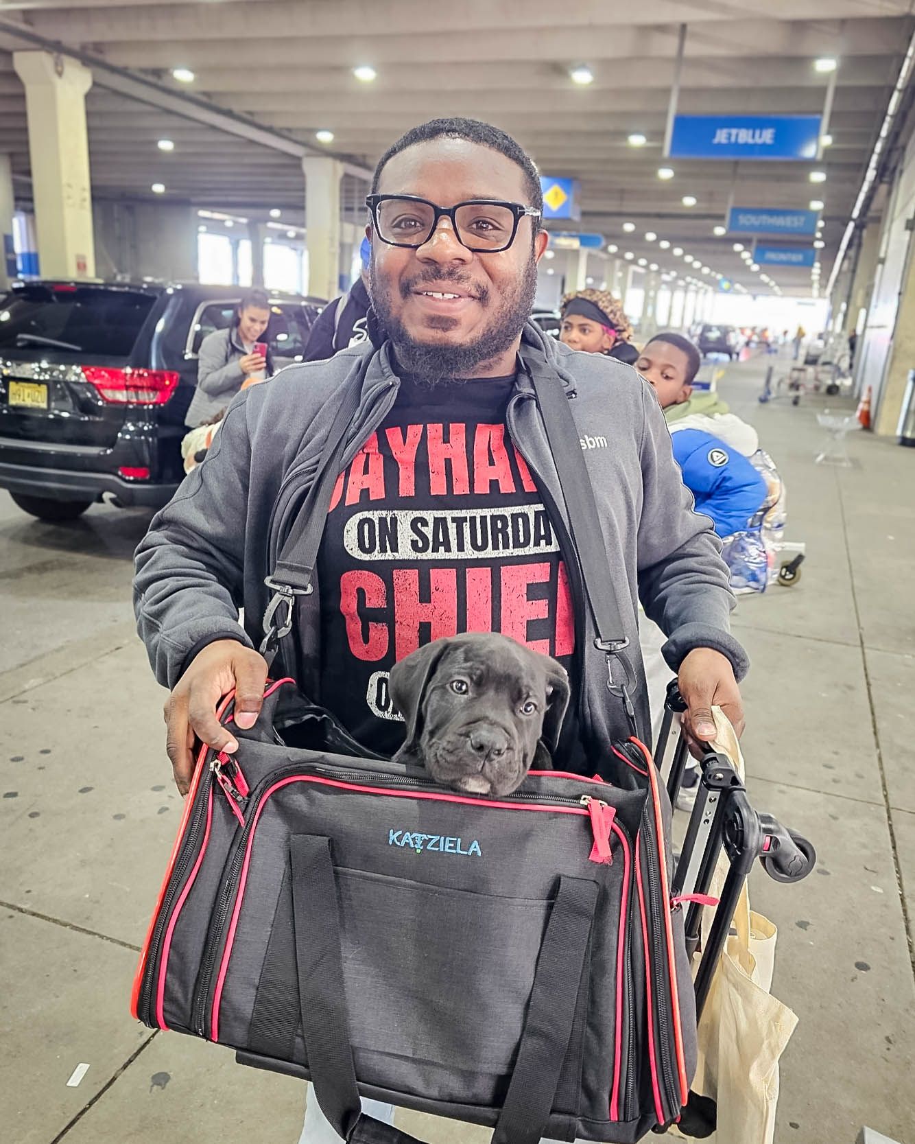 Smiling man holds a Cane Corso puppy in a Katziela pet carrier outside JetBlue airport after pet transport