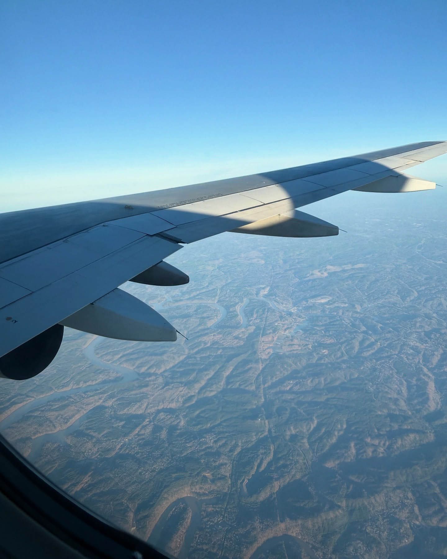 View of airplane wing over mountainous terrain under a clear blue sky during flight nanny service.