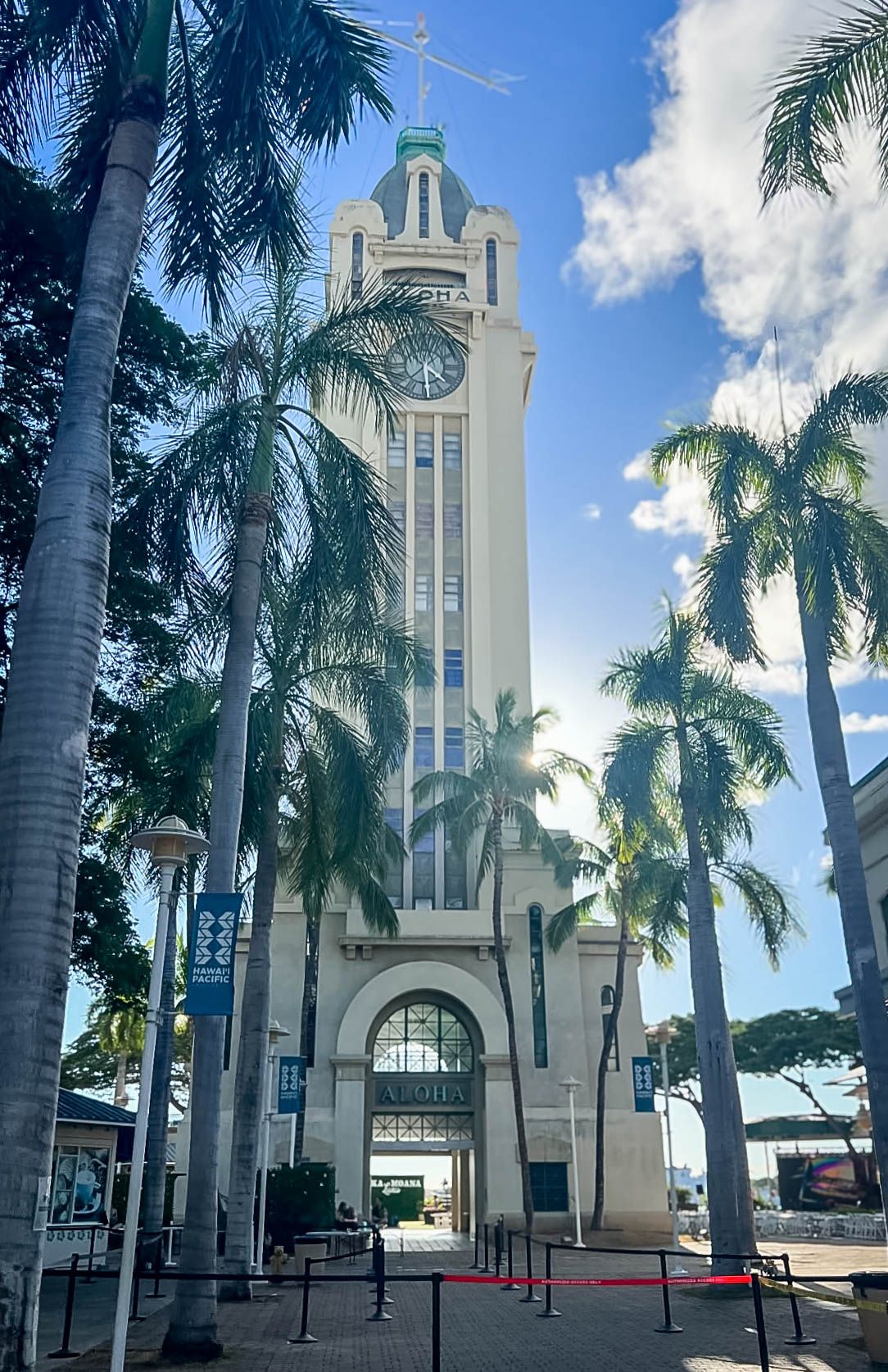 Historic Aloha Tower landmark surrounded by tall palm trees under a blue sky in Honolulu during a layover while doing flight nanny service.