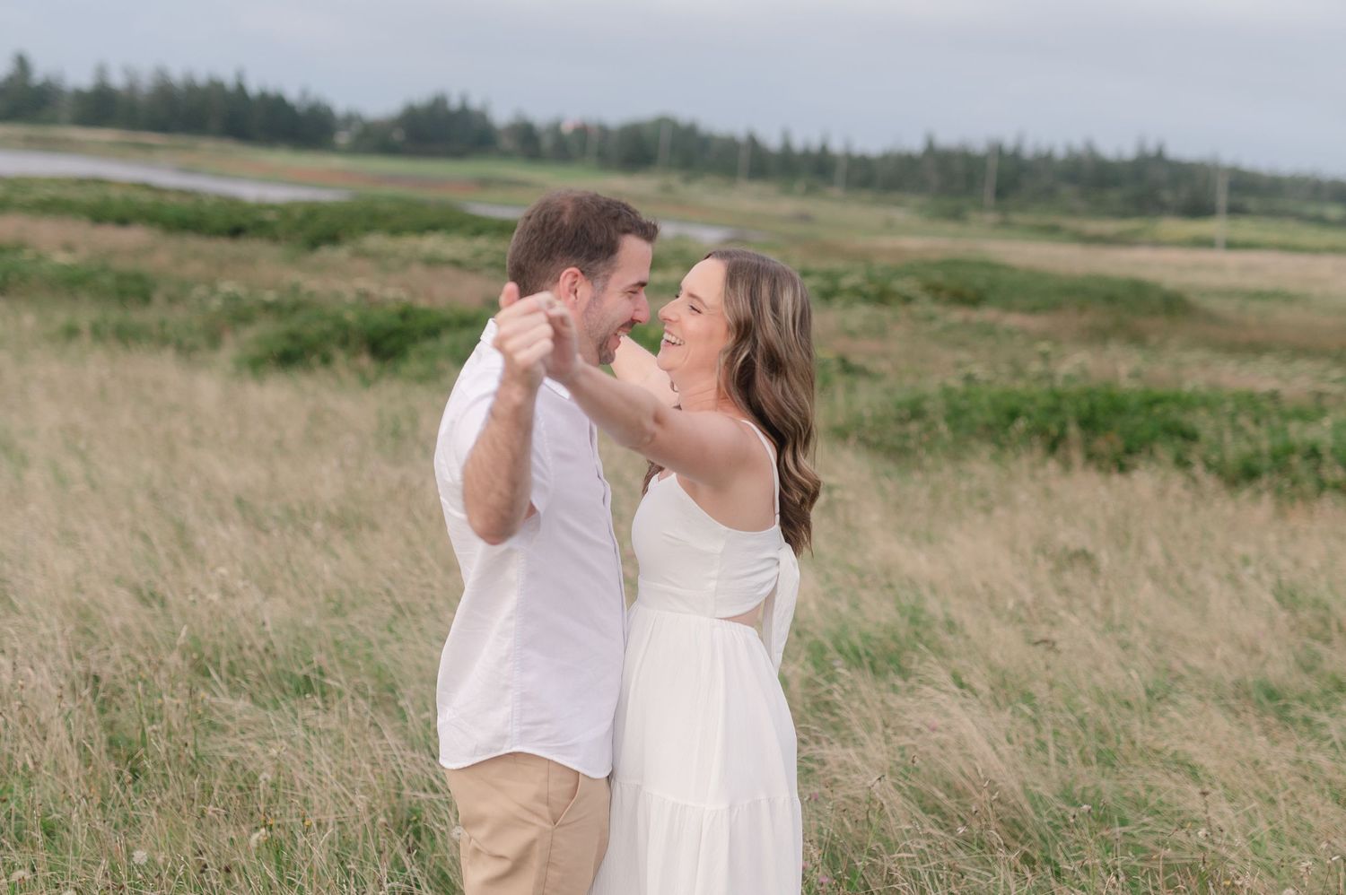 Couple in white and khaki share a tender moment in a grassy meadow.