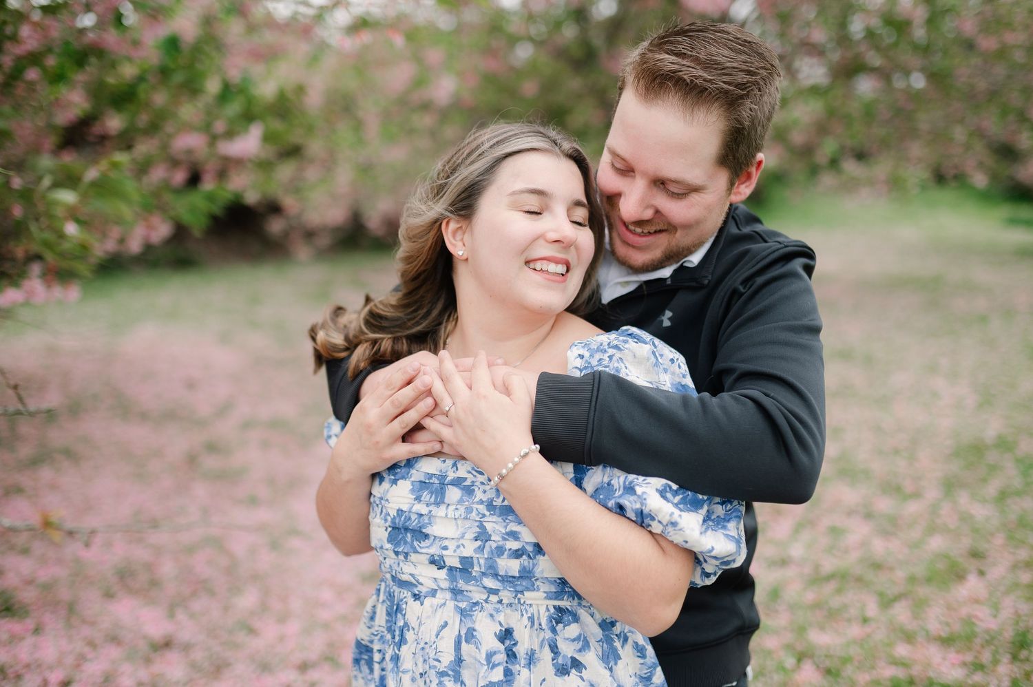 Romantic embrace captured under flowering cherry blossom trees.