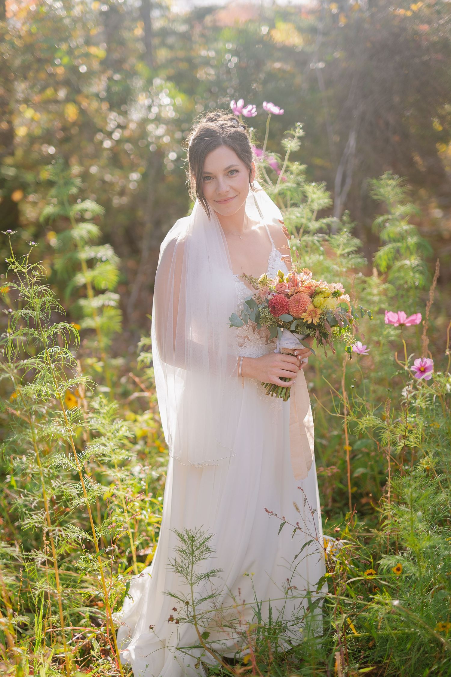 A bride holding a vibrant wildflower bouquet stands among garden flowers in golden evening light.