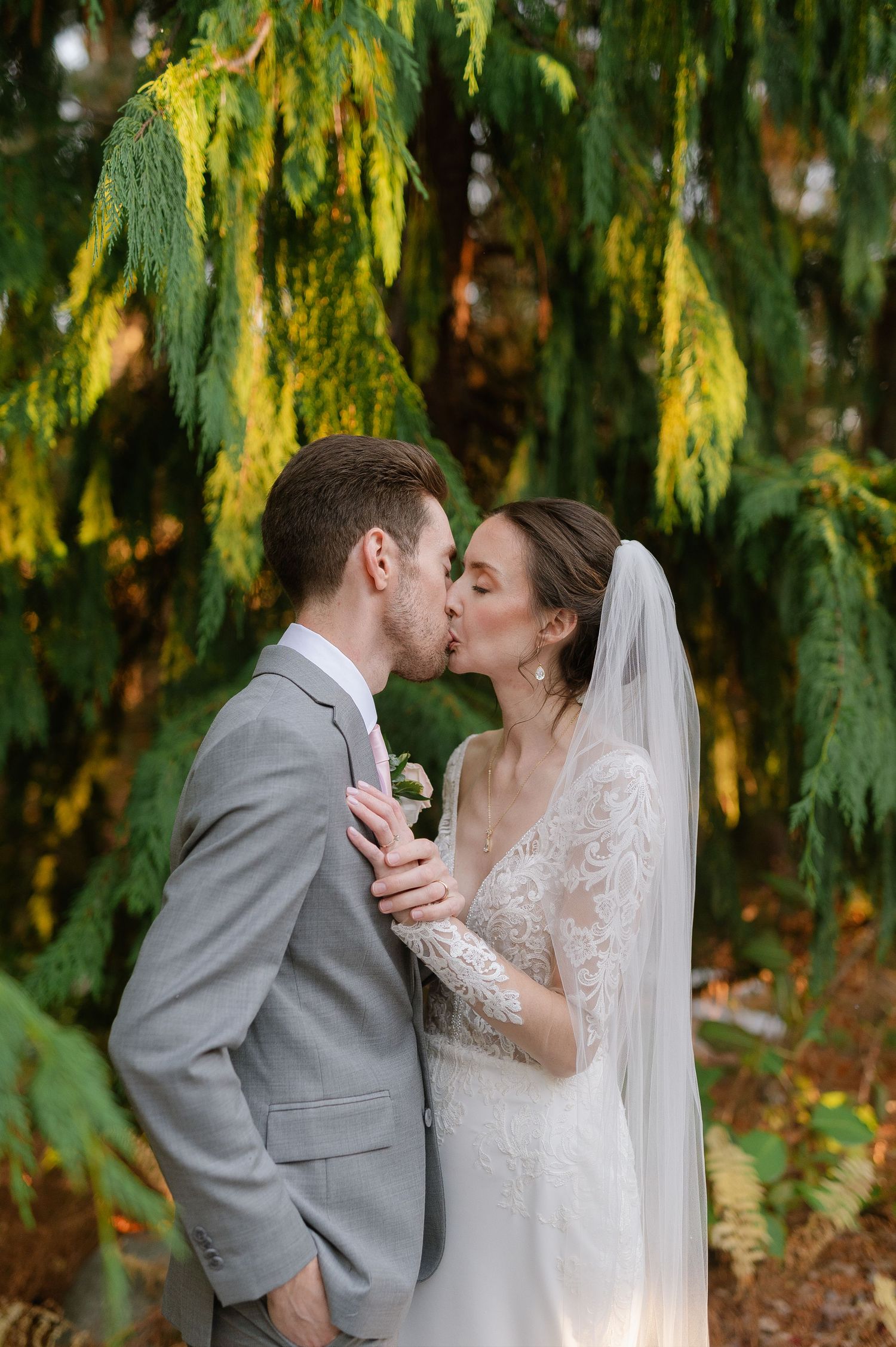 A tender wedding moment captured under weeping willow trees with golden sunlight.